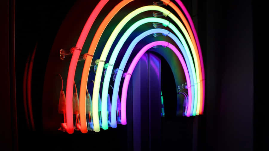 Neon Lights Aesthetic 桌布 壁紙 — 一個充滿活力的彩虹形霓虹燈裝置在黑暗背景中發光，可見電線和燈泡。