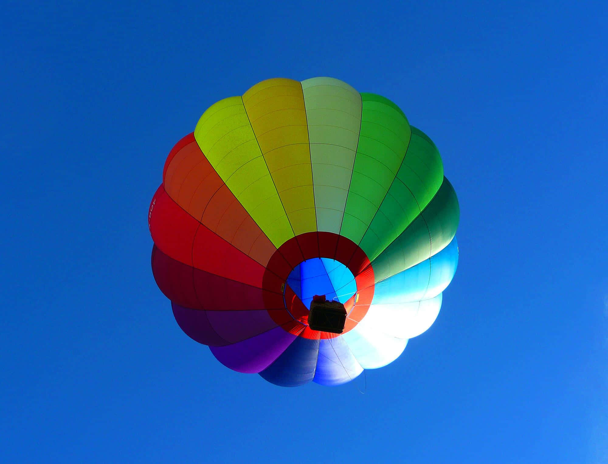 Hot Air Balloon 桌布 壁紙 — 一個充滿活力的彩虹熱氣球在清澈的藍天上寧靜地漂浮。