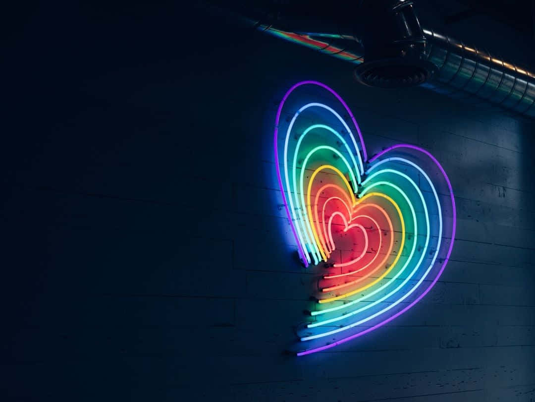 Pride Aesthetic 桌布 壁紙 — 一個充滿活力的彩虹霓虹心臟在工業閣樓環境的深色磚牆上發光。
