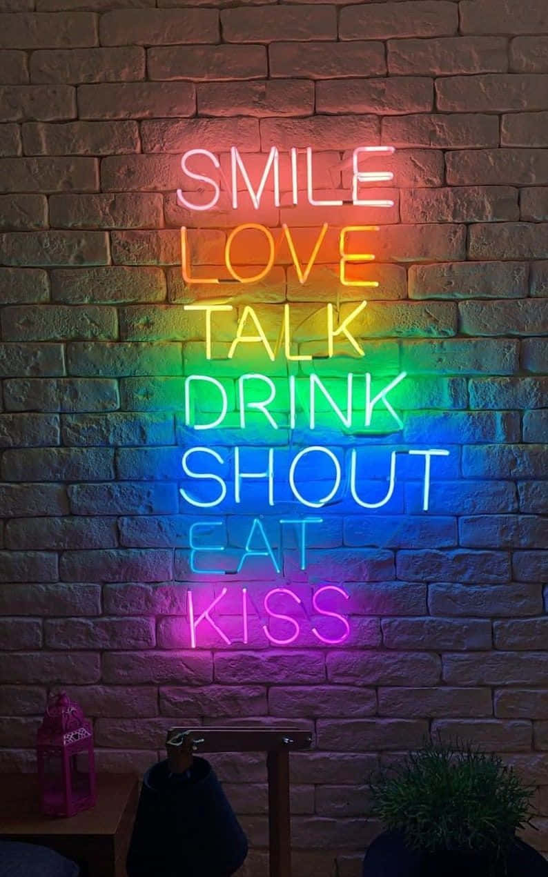Neon Quotes 桌布 壁紙 — 一個充滿活力的彩虹霓虹燈牌，上面有 smile love talk drink shout eat kiss 等字樣，在紋理磚牆上發光。