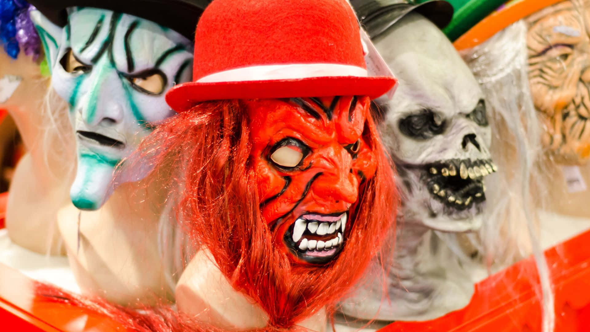 Horror Masks 桌布 壁紙 — 一個充滿活力的恐怖面具展示，包括一個戴著高帽的紅色惡魔和一個骷髏面具，排列在色彩繽紛的商店櫥窗中。