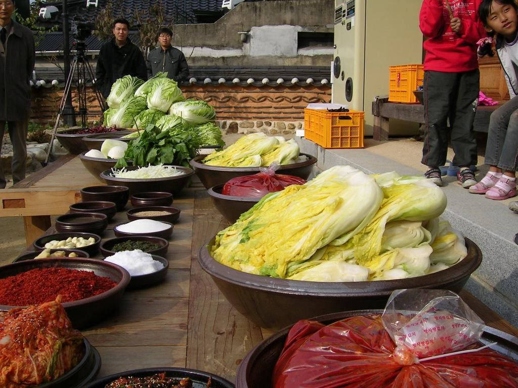 Dish 桌布 壁紙 — 一個充滿活力的戶外場景，木桌上擺放著大碗的新鮮大白菜和色彩繽紛的韓國泡菜配料。