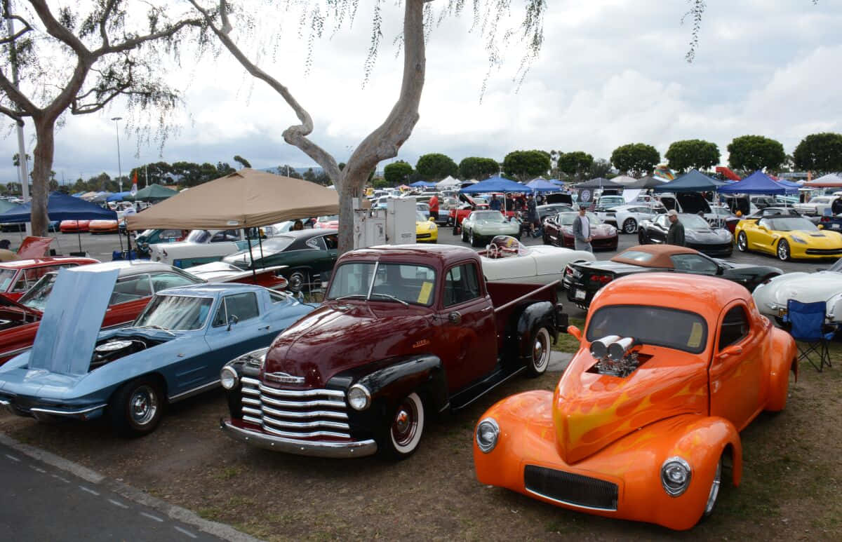 Vintage Car 桌布 壁紙 — 一個充滿活力的戶外車展，在陰天、綠樹成蔭和攤位帳篷下展示經典和定製的熱棒車。