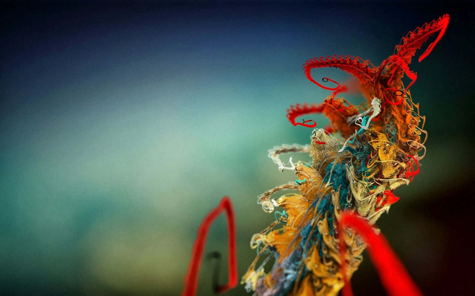 Photography Desktop 桌布 壁紙 — 一個充滿活力的抽象雕塑，由糾纏的紅色、橙色和藍色線條組成，背景是模糊的藍綠色和深藍色。