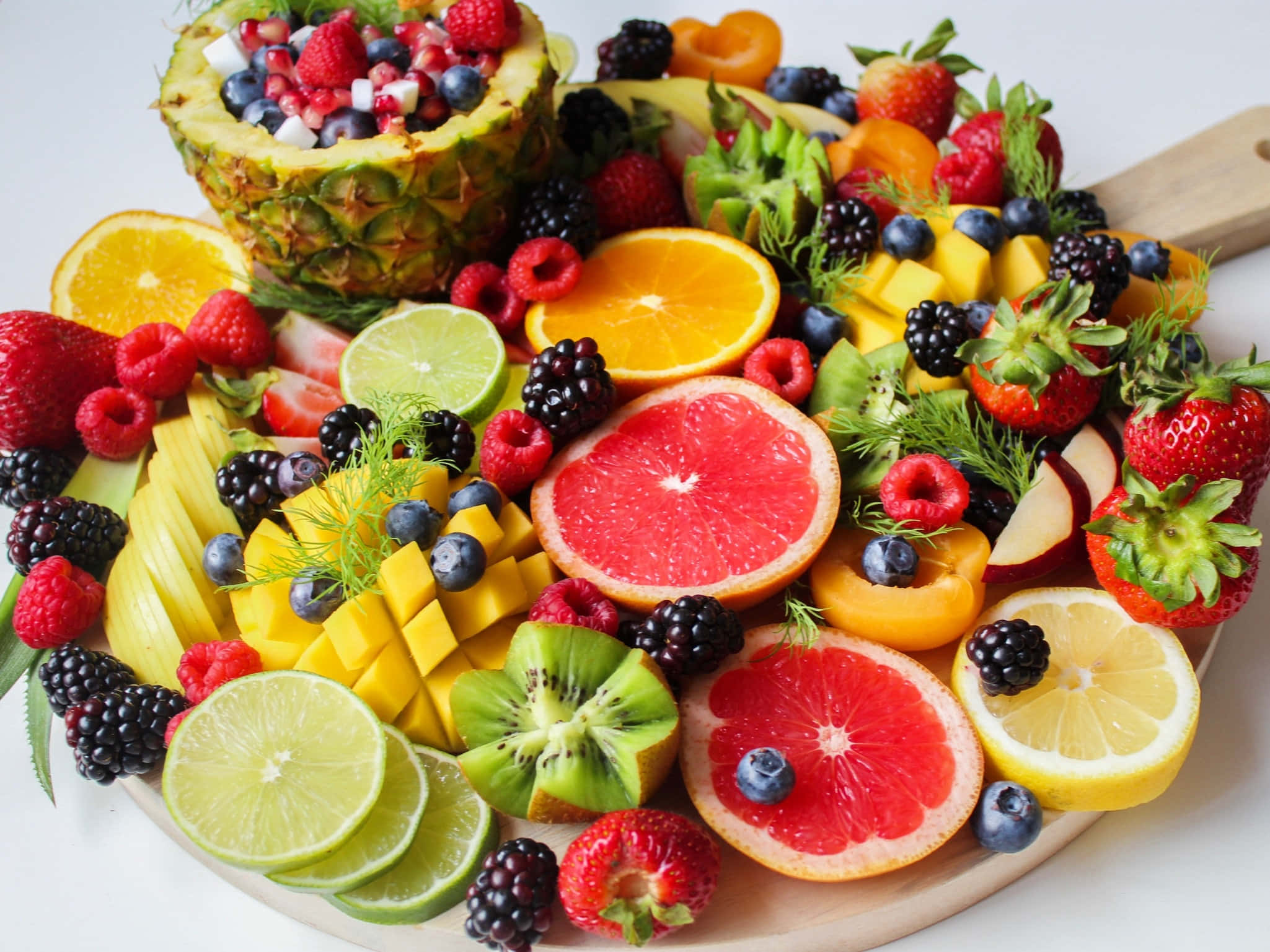 Summer Fruits 桌布 壁紙 — 一個充滿活力的拼盤，上面擺滿了色彩繽紛的切片水果，如鳳梨、葡萄柚和草莓，整齊地排列在木板上。