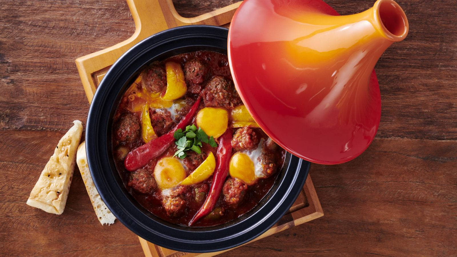 Delicious Food 桌布 壁紙 — 一個充滿活力的摩洛哥塔吉鍋，裡面有肉、甜椒和雞蛋，在木板上一個光亮的紅色陶瓷鍋中冒著蒸氣。