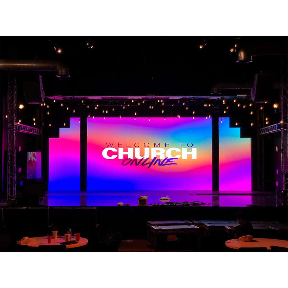 Church Stage 桌布 壁紙 — 一個充滿活力的數位舞台螢幕在燈串下，以粉紅、藍色和紫色的漸變為背景，顯示「WELCOME TO CHURCH ONLINE」。