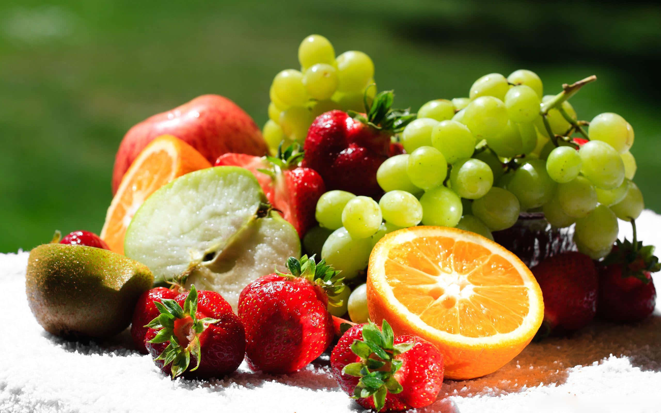 Fruits 桌布 壁紙 — 一個充滿活力的新鮮水果靜物畫，包括草莓、葡萄和柳橙，排列在雪地上，背景是模糊的綠色。