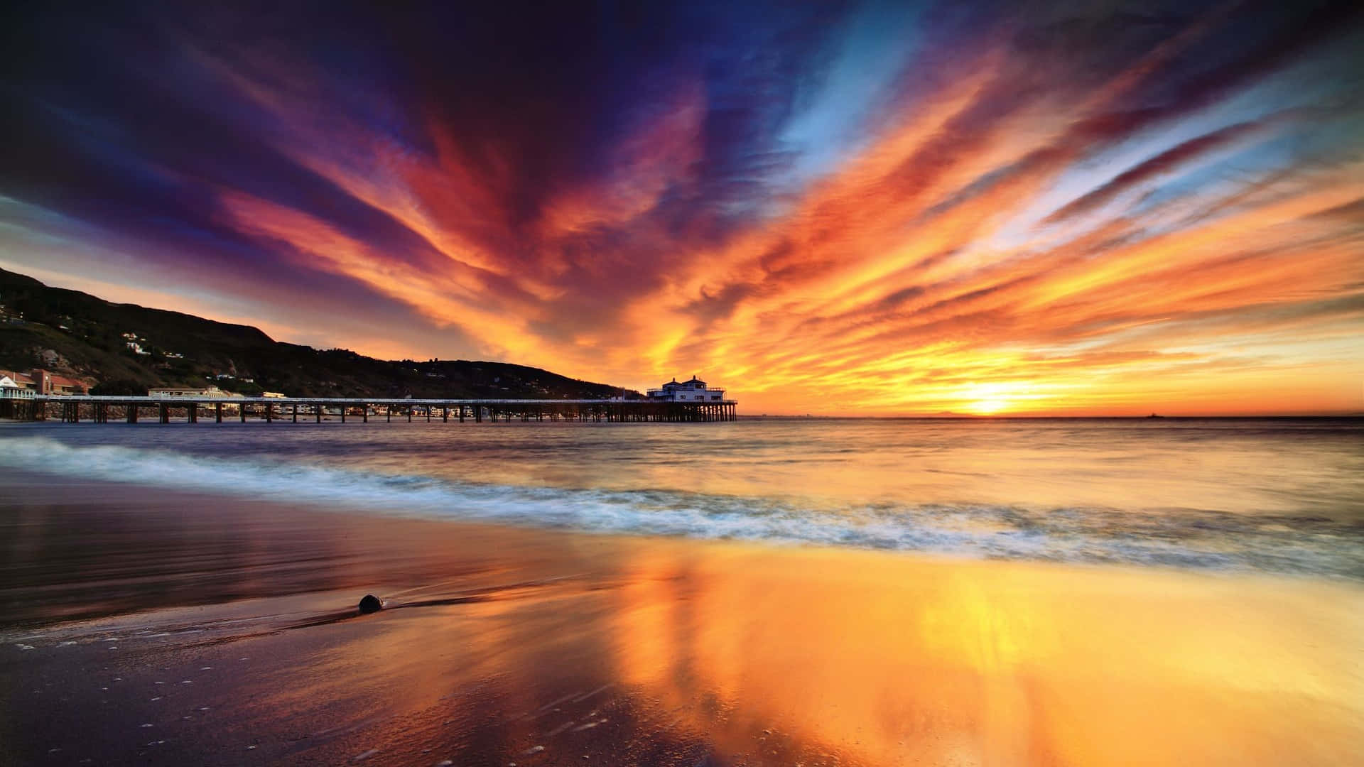 Colorful Sky 桌布 壁紙 — 一個充滿活力的日落將天空染成火熱的橙色和紫色，下方是延伸至平靜海水的長長碼頭。