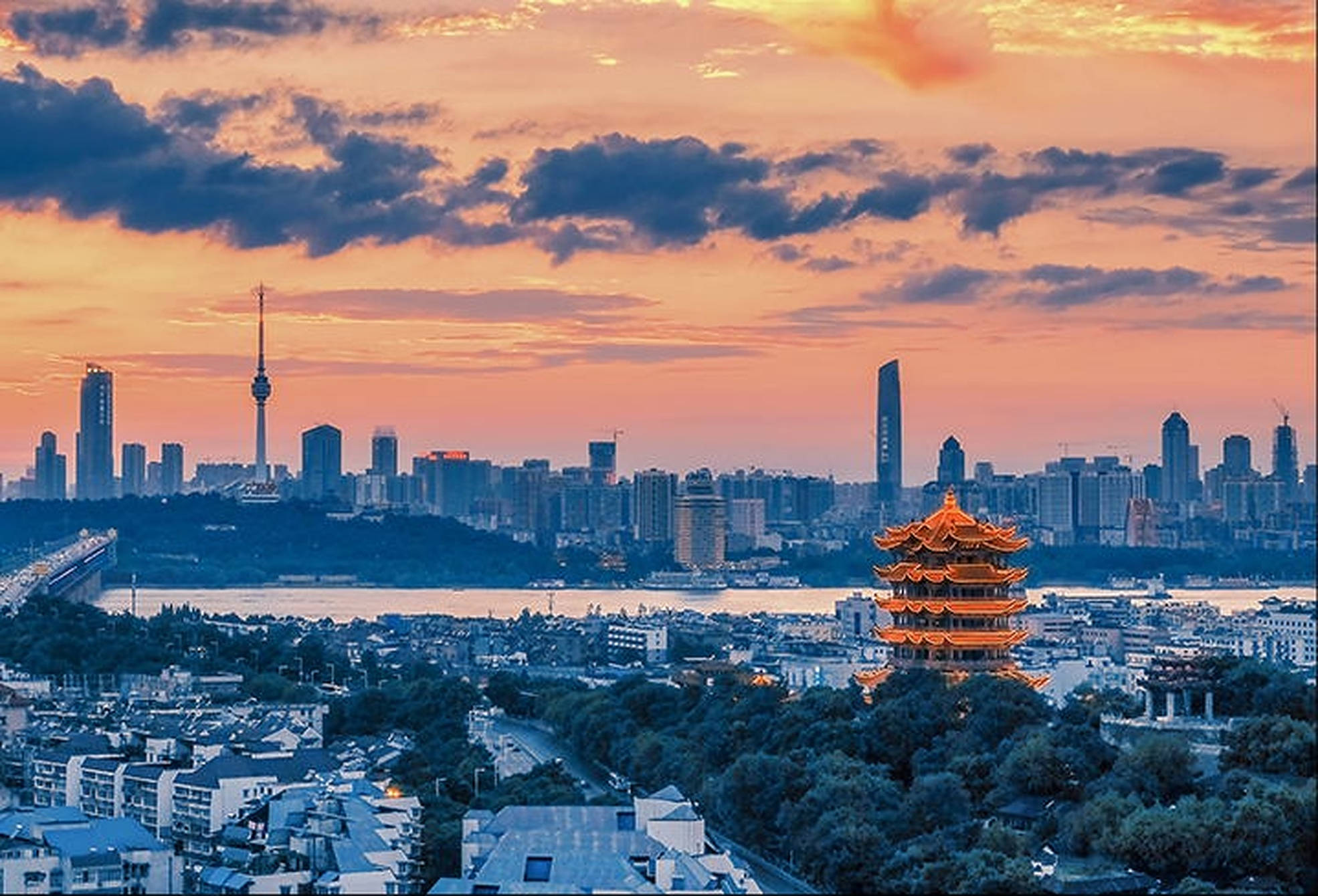 Wuhan 桌布 壁紙 — 一個充滿活力的日落沐浴著現代城市景觀，一座發光的傳統寶塔俯瞰河流和天際線。