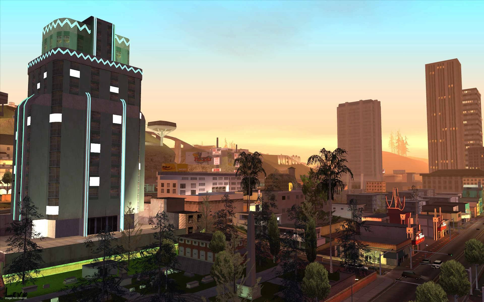 Gta 桌布 壁紙 — 一個充滿活力的日落照耀著一個風格化的城市景觀，特色是霓虹燈閃爍的摩天大樓、棕櫚樹和遠處帶有標誌性好萊塢標誌的山丘。