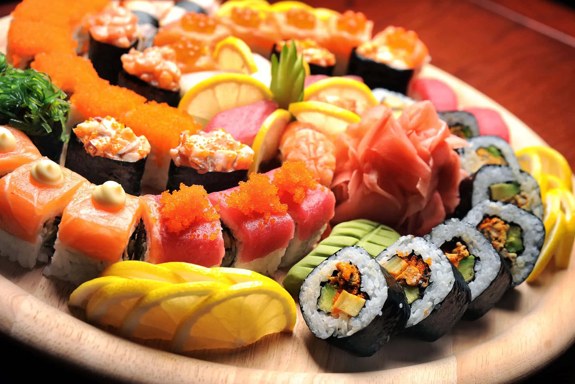 Sushi 桌布 壁紙 — 一個充滿活力的木盤，上面堆滿了色彩繽紛的壽司卷、生魚片和裝飾，在溫暖的燈光下。