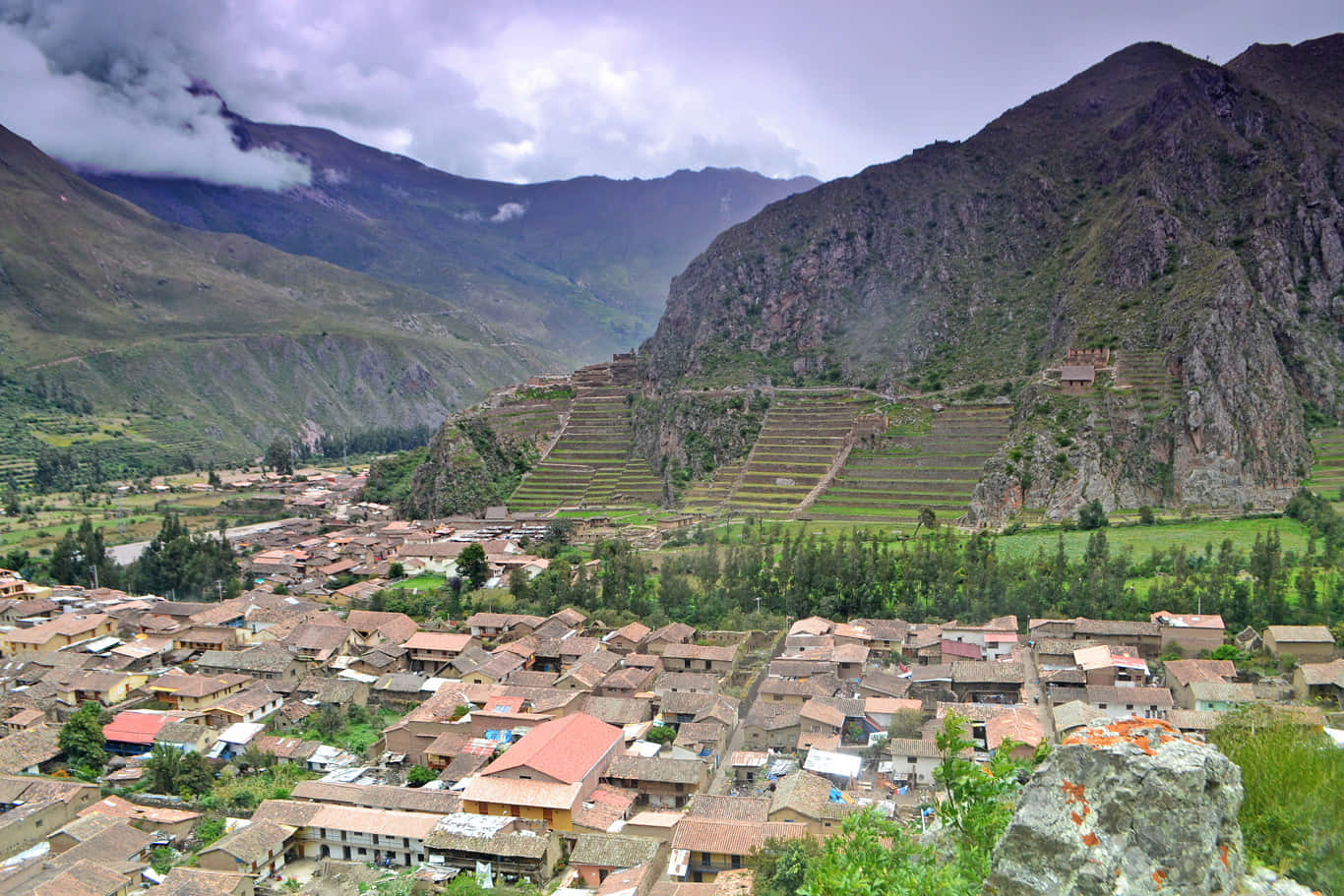 Valley 桌布 壁紙 — 一個充滿活力的村莊坐落在山谷中，梯田石場在陰雲密佈的天空下攀爬陡峭的山坡。