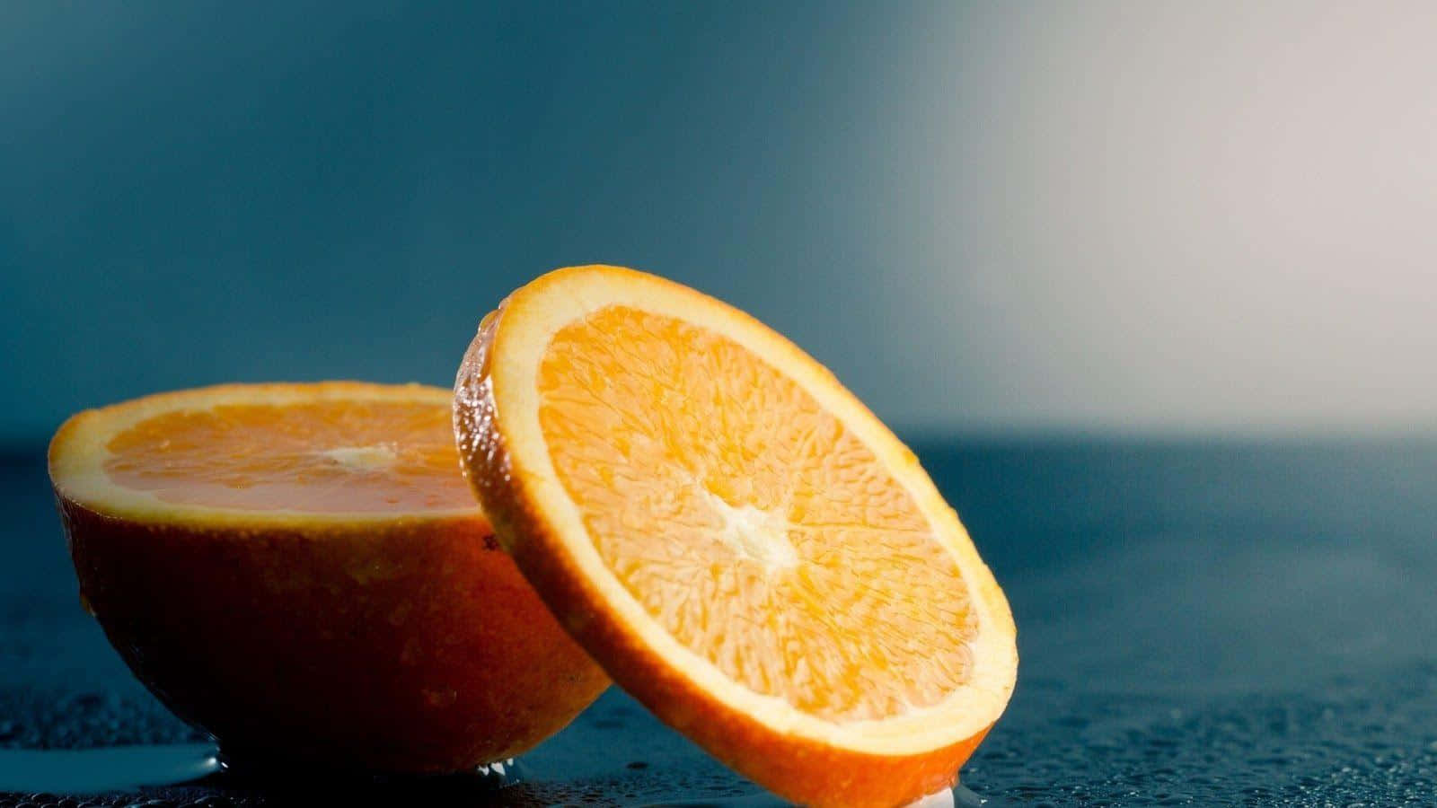 Orange Fruit 桌布 壁紙 — 一個充滿活力的柳橙切半，在清涼的藍色漸層背景上露出多汁的果肉。