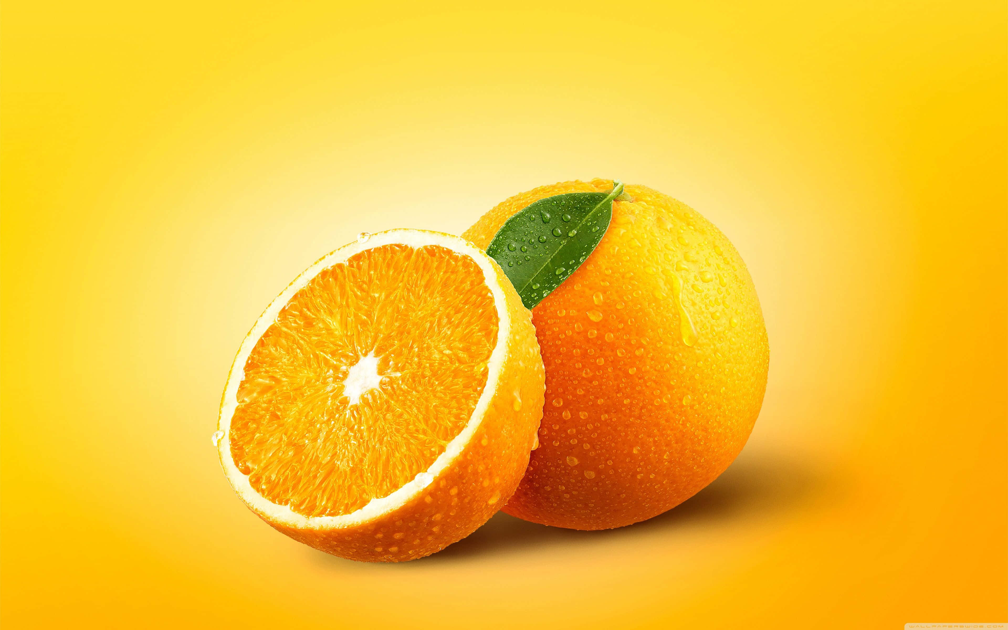 Orange Desktop 桌布 壁紙 — 一個充滿活力的柳橙切半，旁邊放著一個完整的柳橙，帶有綠葉和水珠，背景是金黃色漸層。