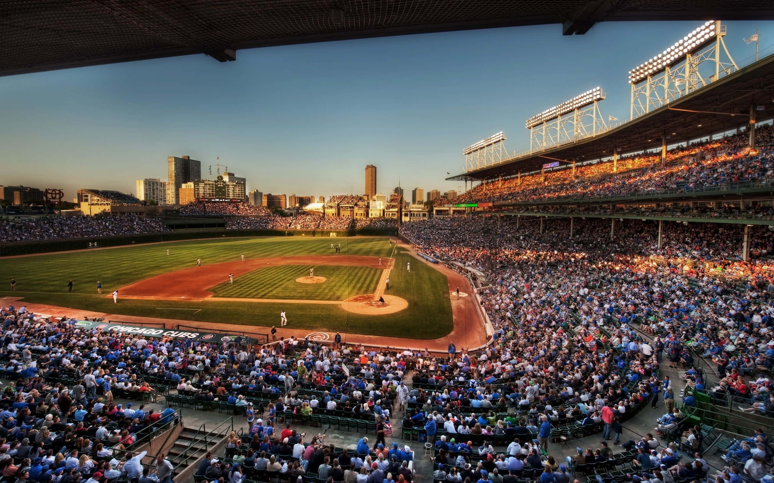 MLB Baseball League 桌布 壁紙 — 一個充滿活力的棒球場，擠滿了歡呼的球迷，背景是金色夕陽天空和城市天際線。
