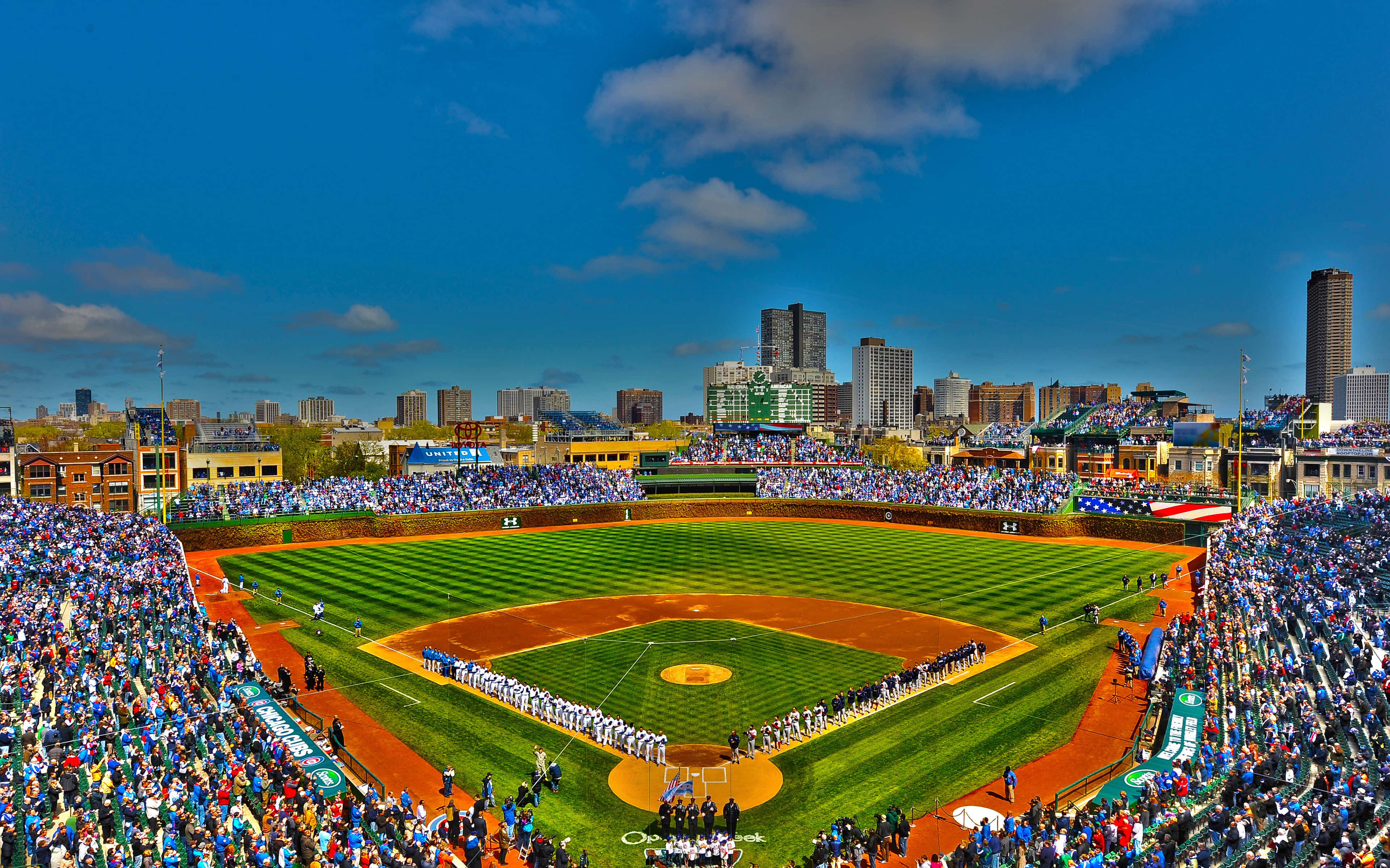 Baseball Stadium 桌布 壁紙 — 一個充滿活力的棒球場，擠滿了球迷，天空湛藍，白雲點綴。