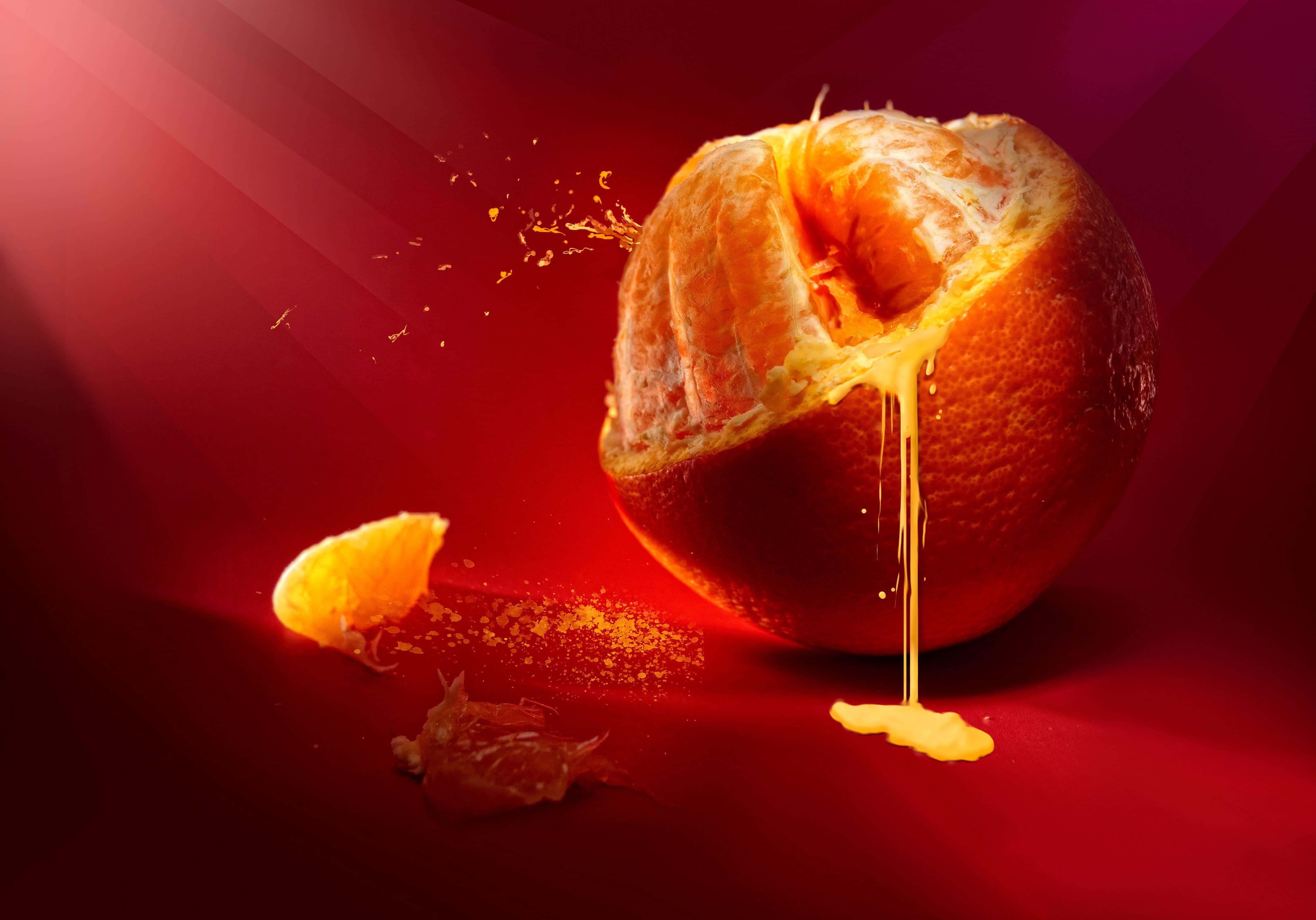 Orange Fruit 桌布 壁紙 — 一個充滿活力的橙子在深紅色漸變背景上爆開，果汁四濺，果皮碎片散落四周。