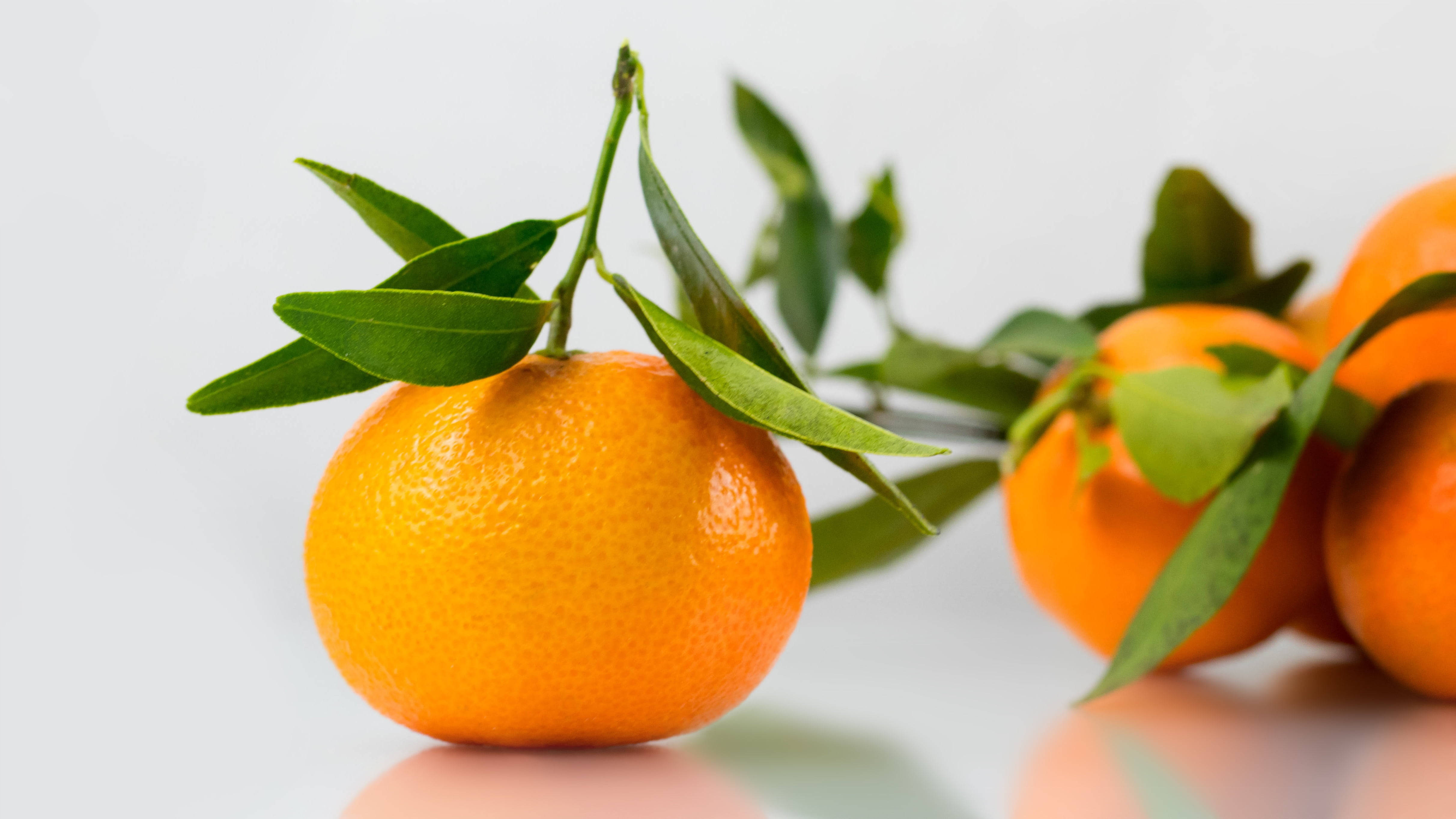 Fruits 桌布 壁紙 — 一個充滿活力的橙色柑橘，帶有新鮮的綠葉，在乾淨的白色背景上清晰對焦，帶有柔和的反光。