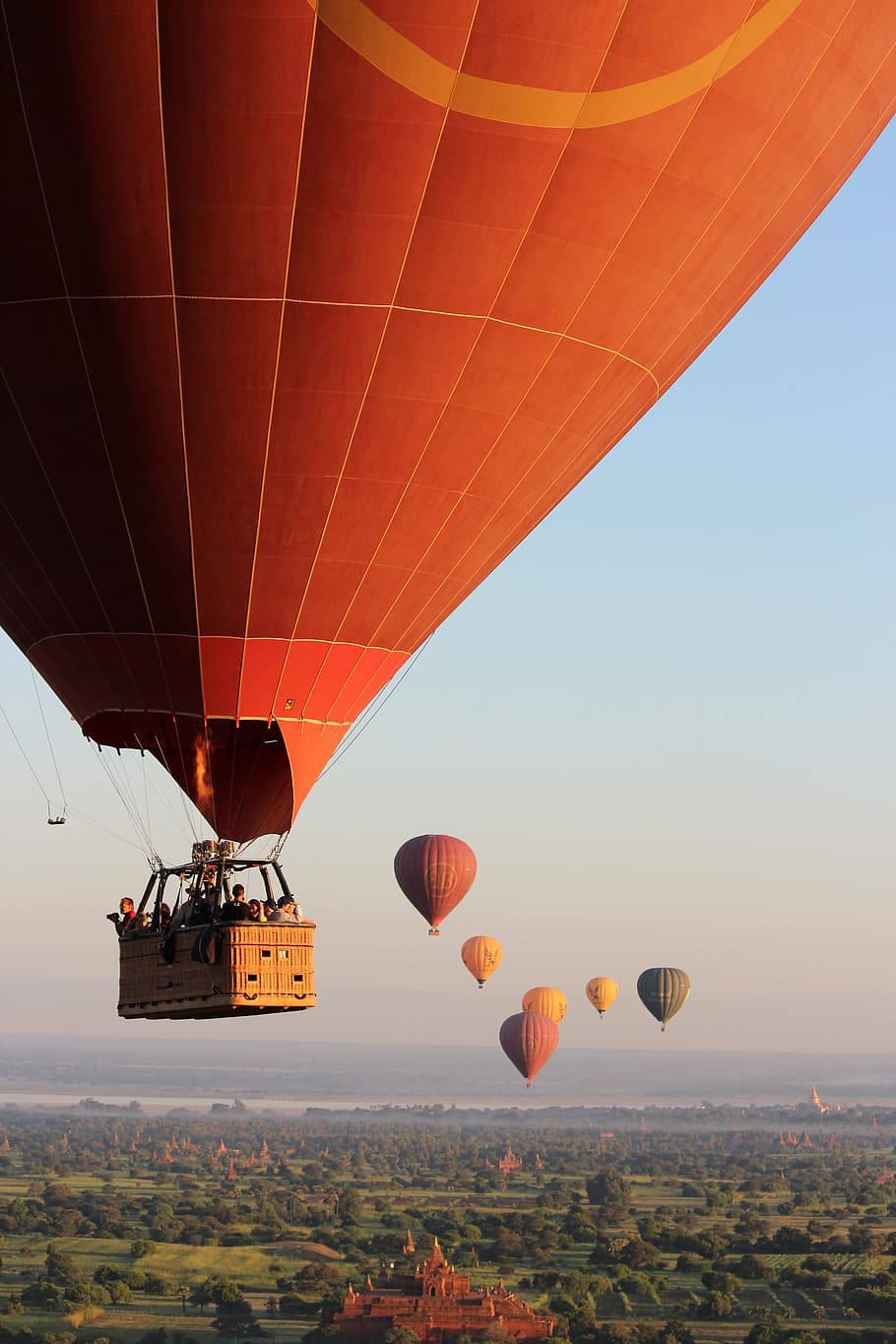 Hot Air Balloon 桌布 壁紙 — 一個充滿活力的橙色熱氣球在日出時分飄浮在點綴著古老寺廟的廣闊景觀之上，主導了畫面。