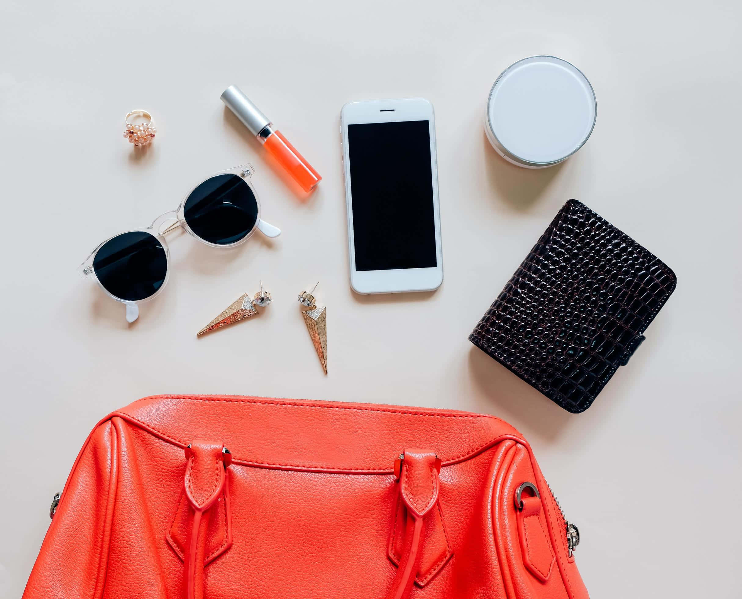 Red Handbag 桌布 壁紙 — 一個充滿活力的橙色皮革手提包放在中央，太陽眼鏡、口紅、電話和配件整齊地排列在淺米色表面上。