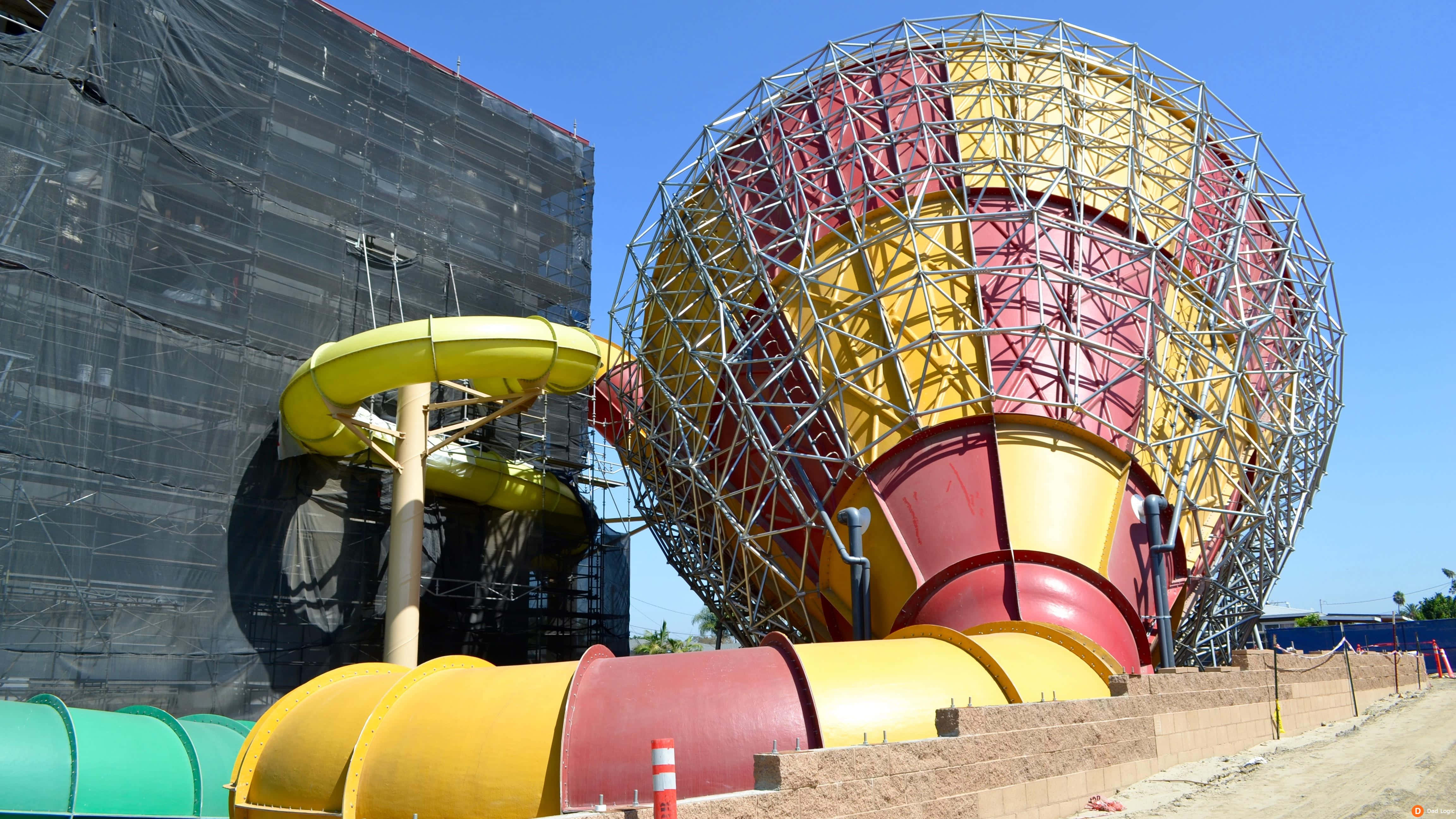 great wolf lodge 桌布 壁紙 — 一個充滿活力的水上樂園正在建設中，設有一個巨大的紅黃色滑梯結構和一個黃色螺旋滑梯，背景是晴朗的藍天。