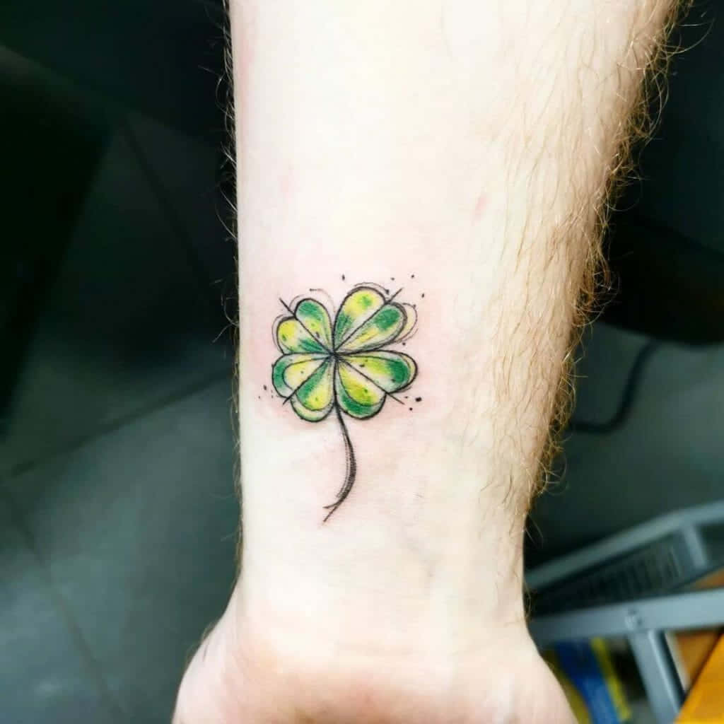 Four Leaf Clover 桌布 壁紙 — 一個充滿活力的水彩四葉草刺青，位於多毛的前臂上，帶有飛濺的綠色和黃色墨水。