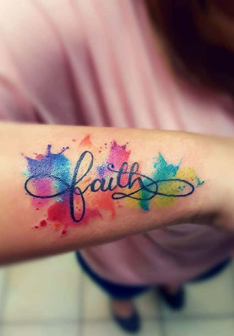 Tattoo 桌布 壁紙 — 一個充滿活力的水彩紋身，以優雅的字體寫著「信仰」一詞，周圍是色彩繽紛的潑濺，位於一個人的前臂內側。