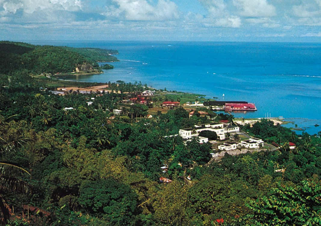 Jamaican Island 桌布 壁紙 — 一個充滿活力的沿海小鎮，坐落在茂密的綠色叢林中，在部分多雲的天空下，碧綠的海洋一直延伸到地平線。