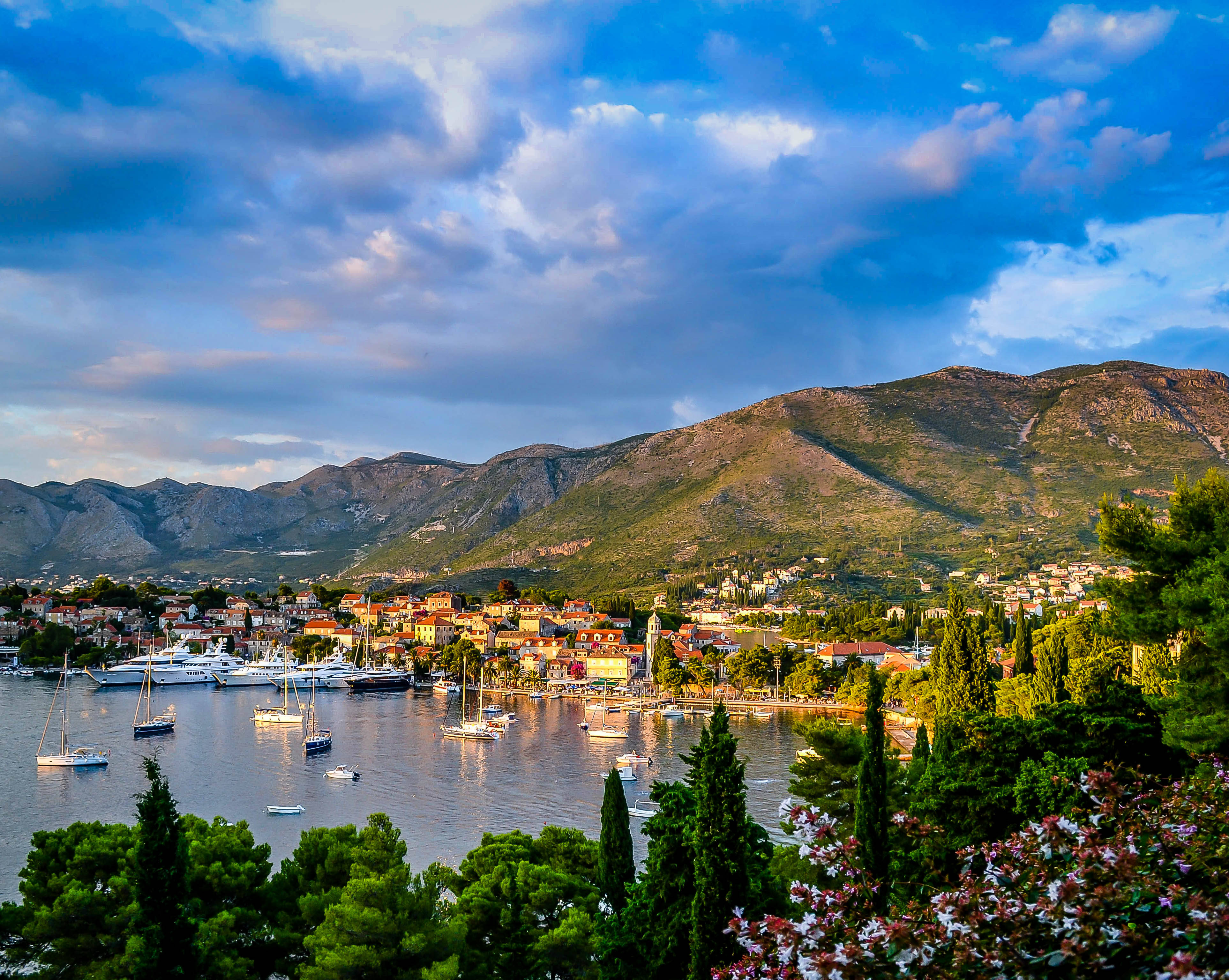 Croatia 桌布 壁紙 — 一個充滿活力的沿海小鎮，坐落於海灣中，背後有山脈在戲劇性的藍天下升起。