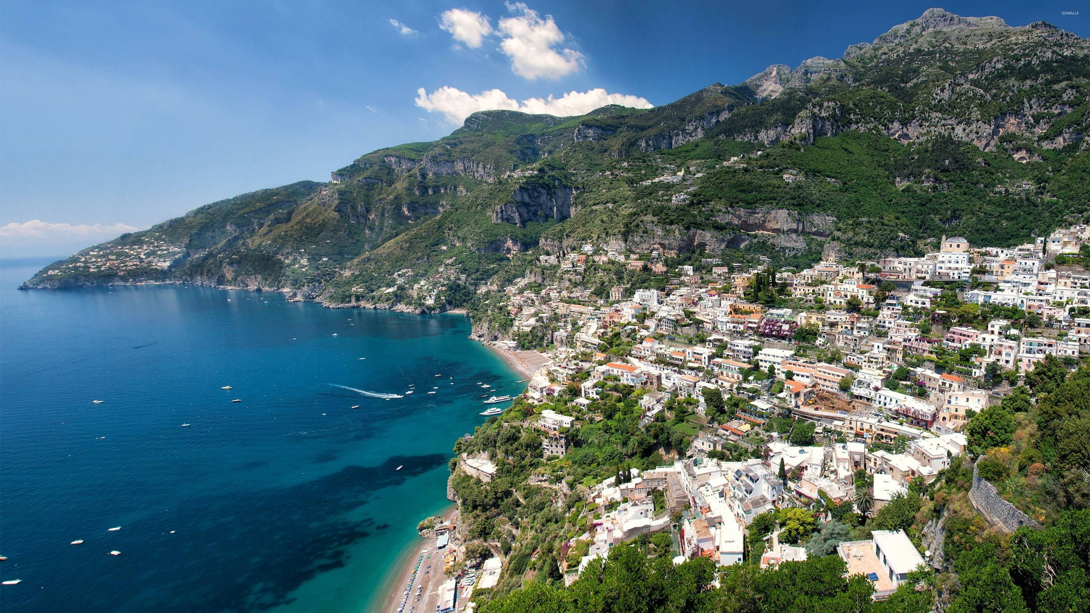 Amalfi Coast 桌布 壁紙 — 一個充滿活力的沿海小鎮依附在陡峭的綠色懸崖上，俯瞰著碧藍的海水，天空湛藍。