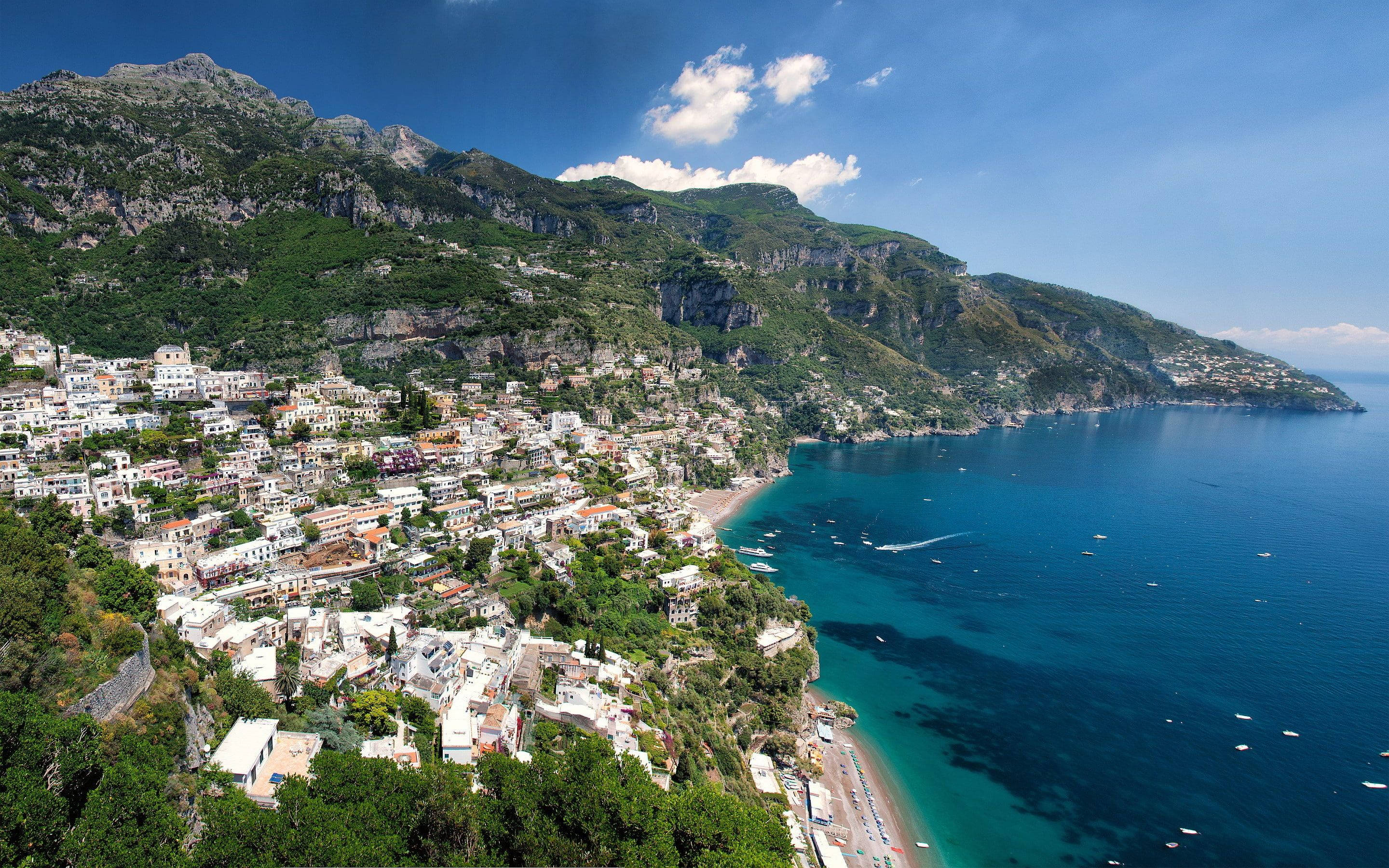 Capri 桌布 壁紙 — 一個充滿活力的沿海小鎮依附在陡峭的綠色懸崖上，俯瞰著湛藍的海水，上方是明亮的藍天。