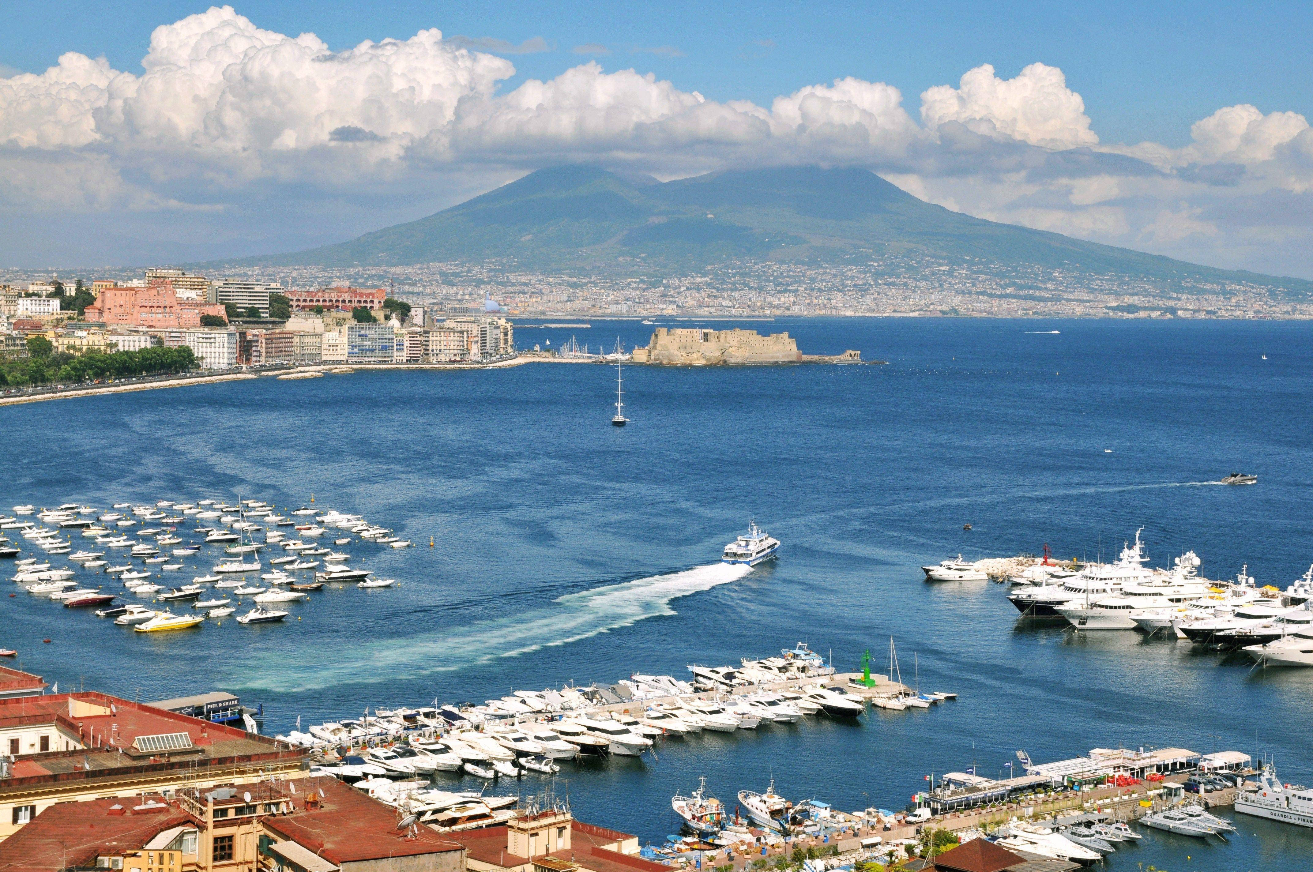 Naples 桌布 壁紙 — 一個充滿活力的沿海港口，停滿了船隻，在明亮的藍天下，遠處是維蘇威火山。
