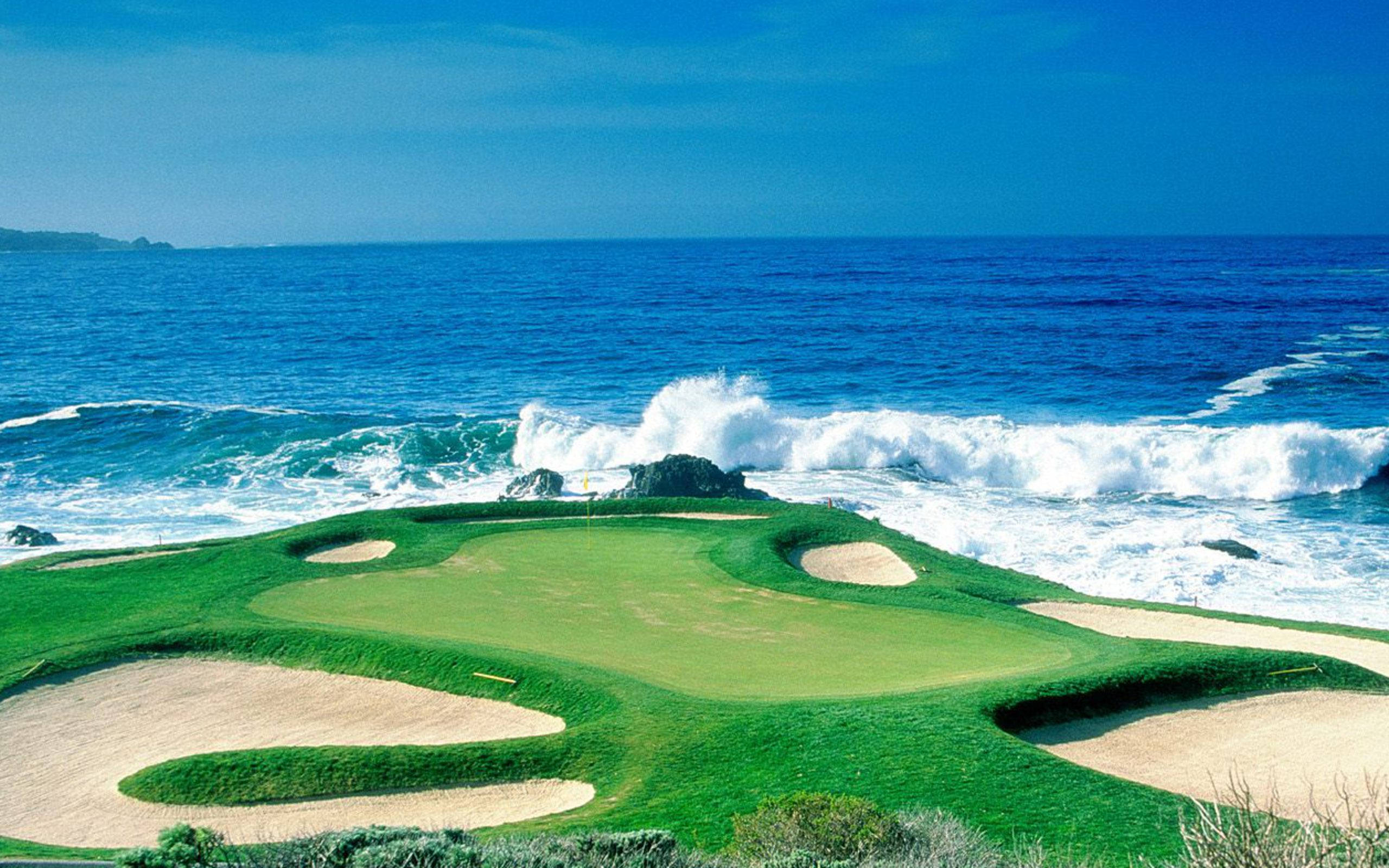 Golf Course 桌布 壁紙 — 一個充滿活力的海岸高爾夫球場，擁有茂密的綠色球道和沙坑，旁邊是清澈藍天下拍打的海浪。