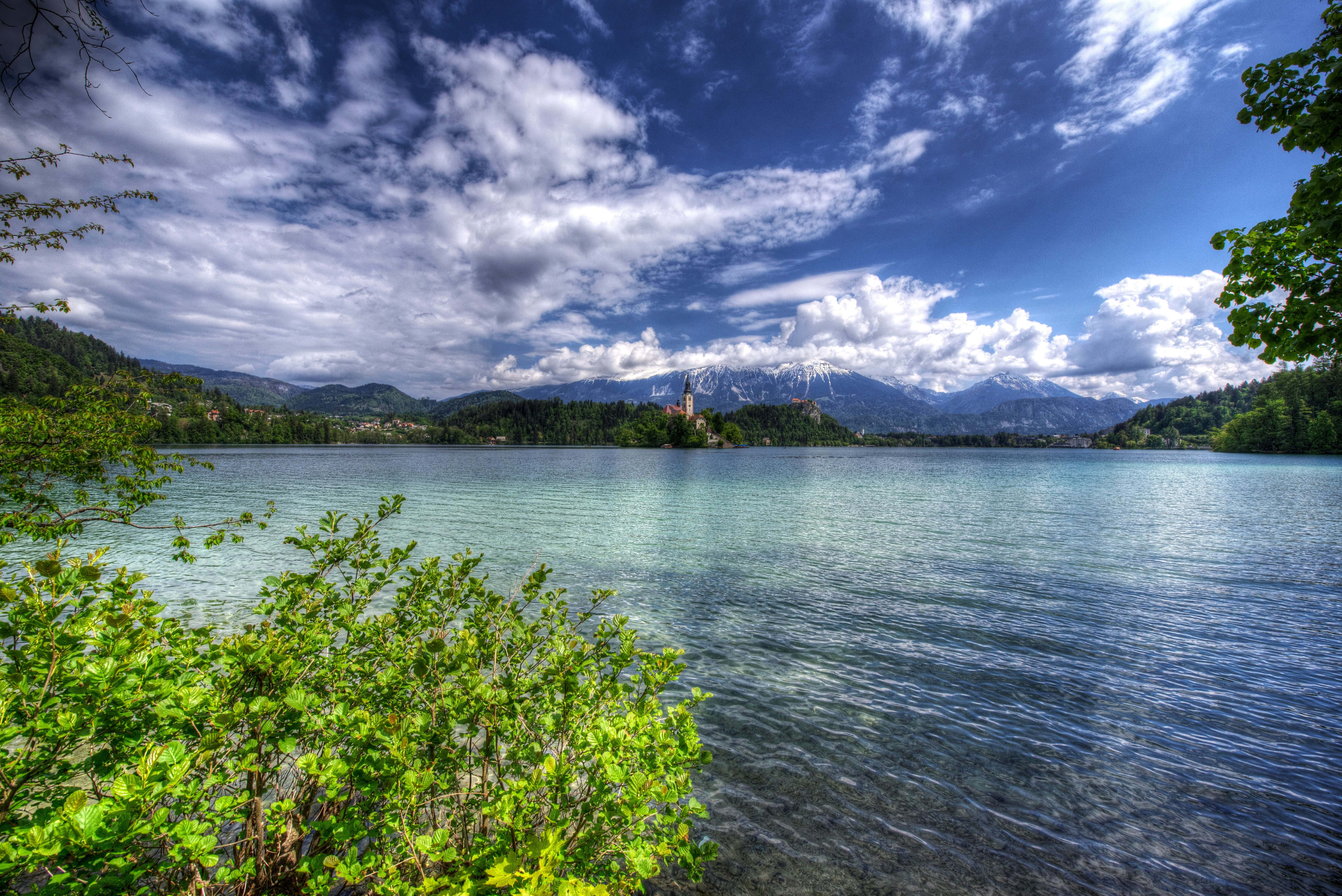 Beautiful Lake 桌布 壁紙 — 一個充滿活力的湖泊，被茂密的綠植環繞，上方是戲劇性的藍天和蓬鬆的白雲。