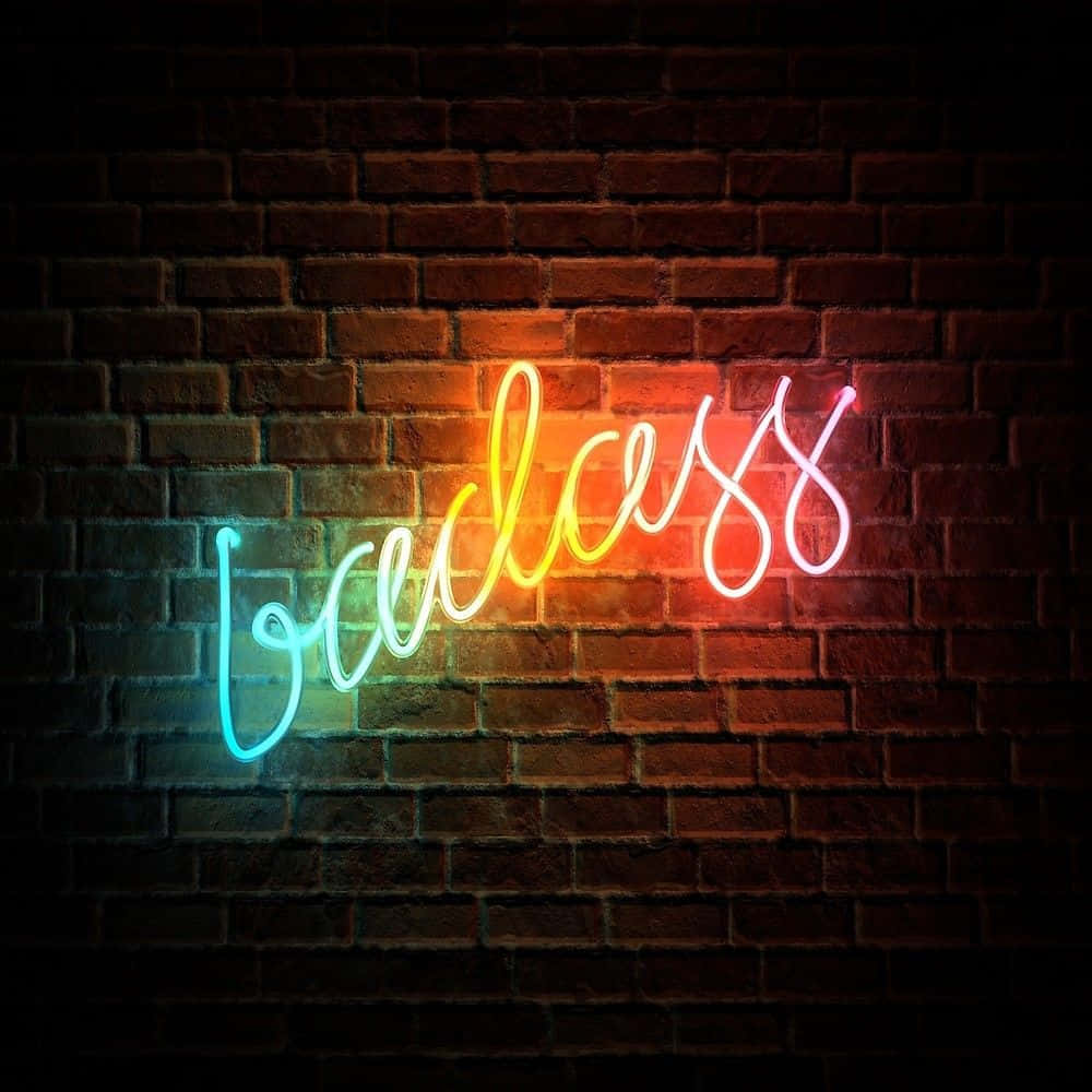 霓虹美學 桌布 壁紙 — 一個充滿活力的漸變霓虹燈牌拼出 'badass'，在黑暗的磚牆上發光，營造出陰鬱的城市氛圍。