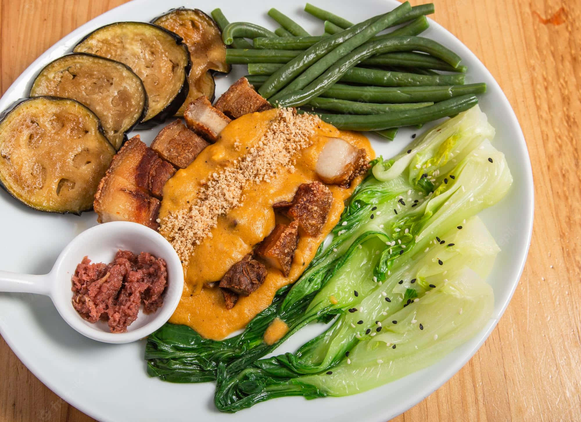 meat 桌布 壁紙 — 一個充滿活力的烤茄子、青豆和脆皮豬肉配奶油醬和芝麻的菜餚，放在木桌上。