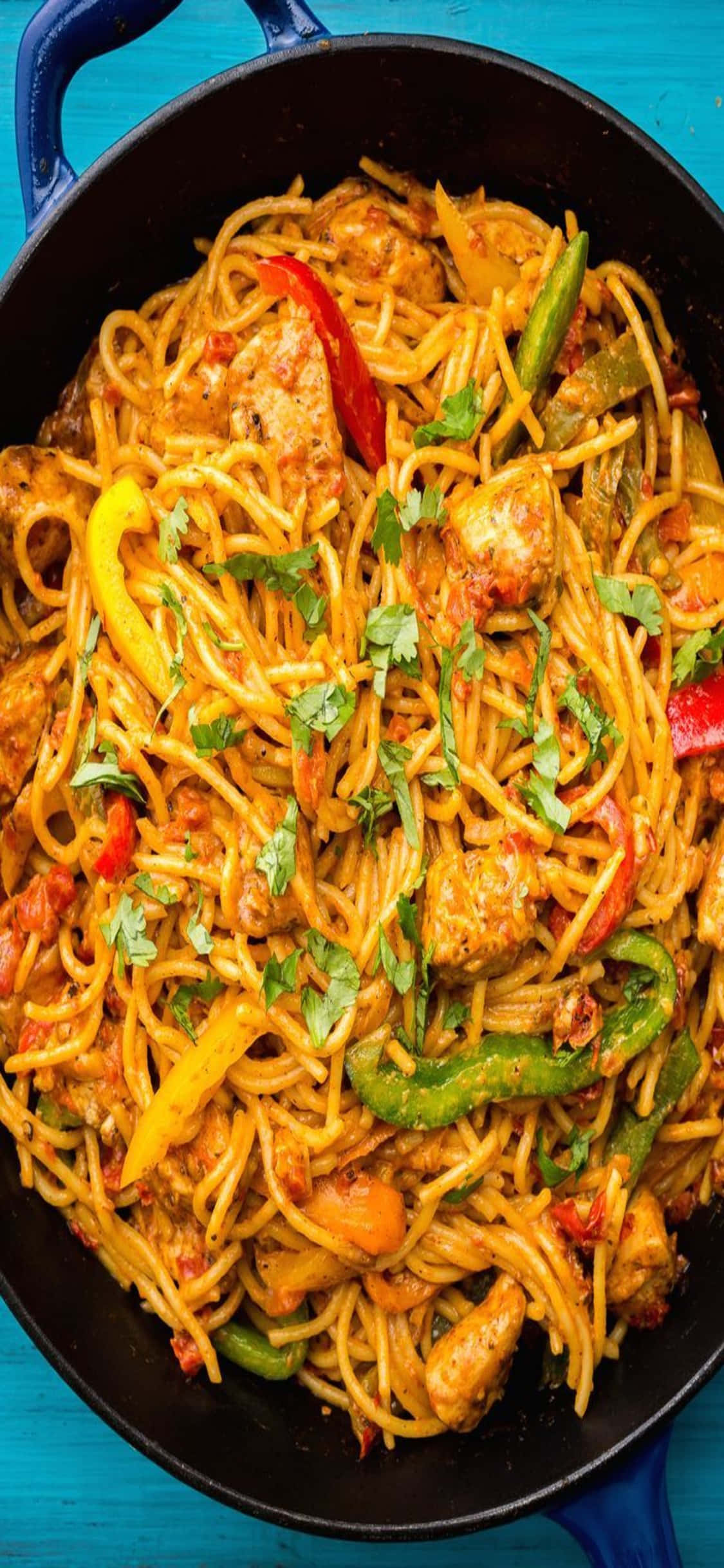 food iPhone 桌布 壁紙 — 一個充滿活力的煎鍋，裝著辣味雞肉義大利麵，配上色彩繽紛的甜椒和新鮮香菜，放在亮藍色的表面上。
