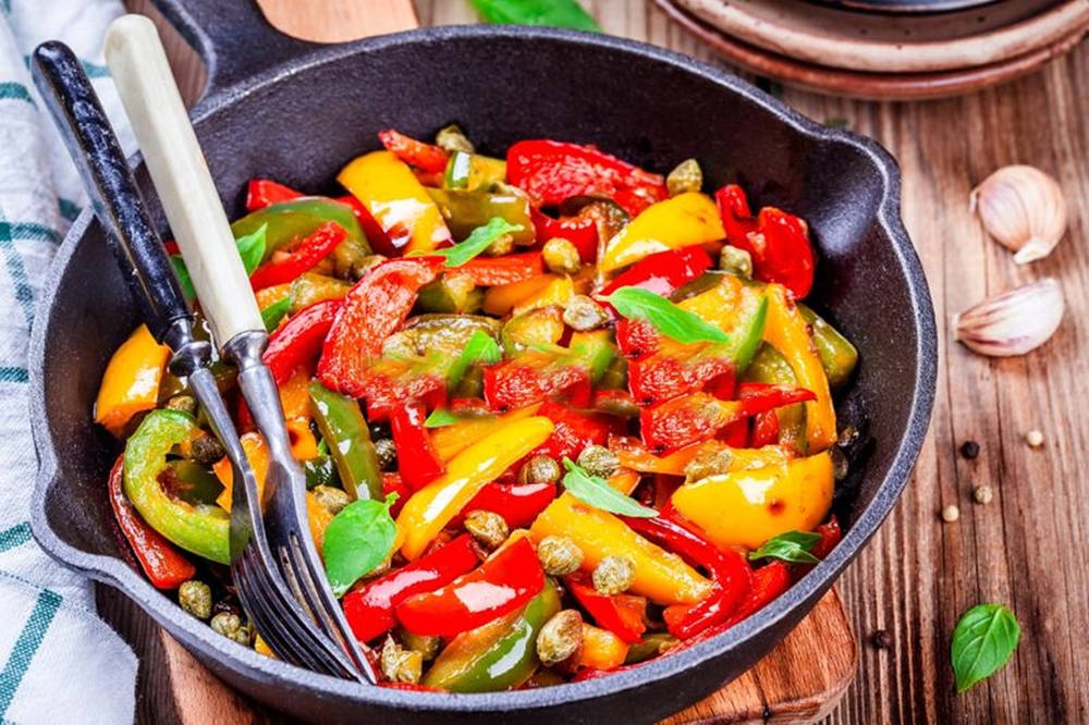 Fruit 桌布 壁紙 — 一個充滿活力的煎鍋，裡面有炒甜椒、酸豆和羅勒，在質樸的木桌上閃爍著油光。