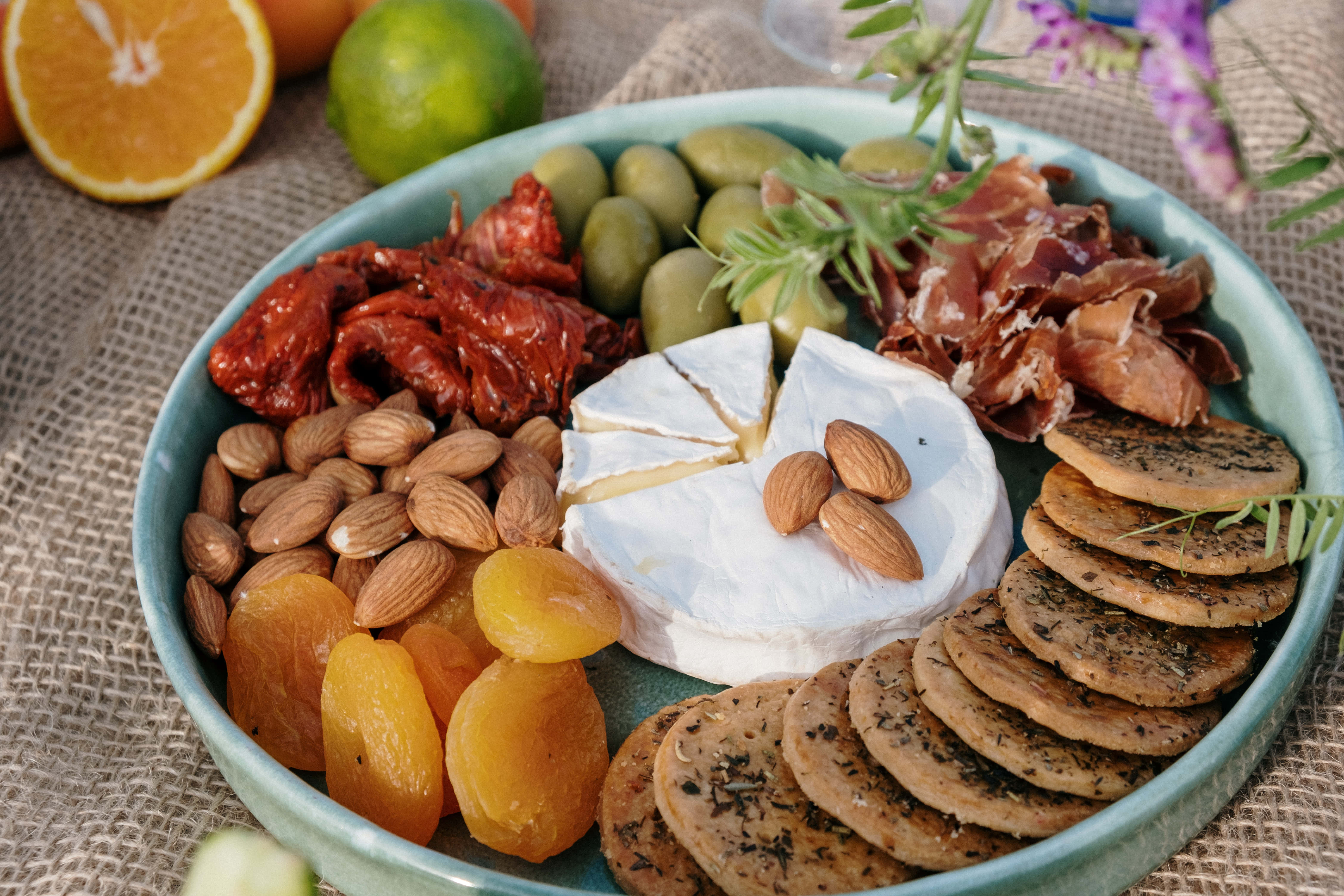 Cheese 桌布 壁紙 — 一個充滿活力的熟食拼盤，上面擺放著起司、杏仁、橄欖和柑橘類水果，置於質樸的黃麻表面上。