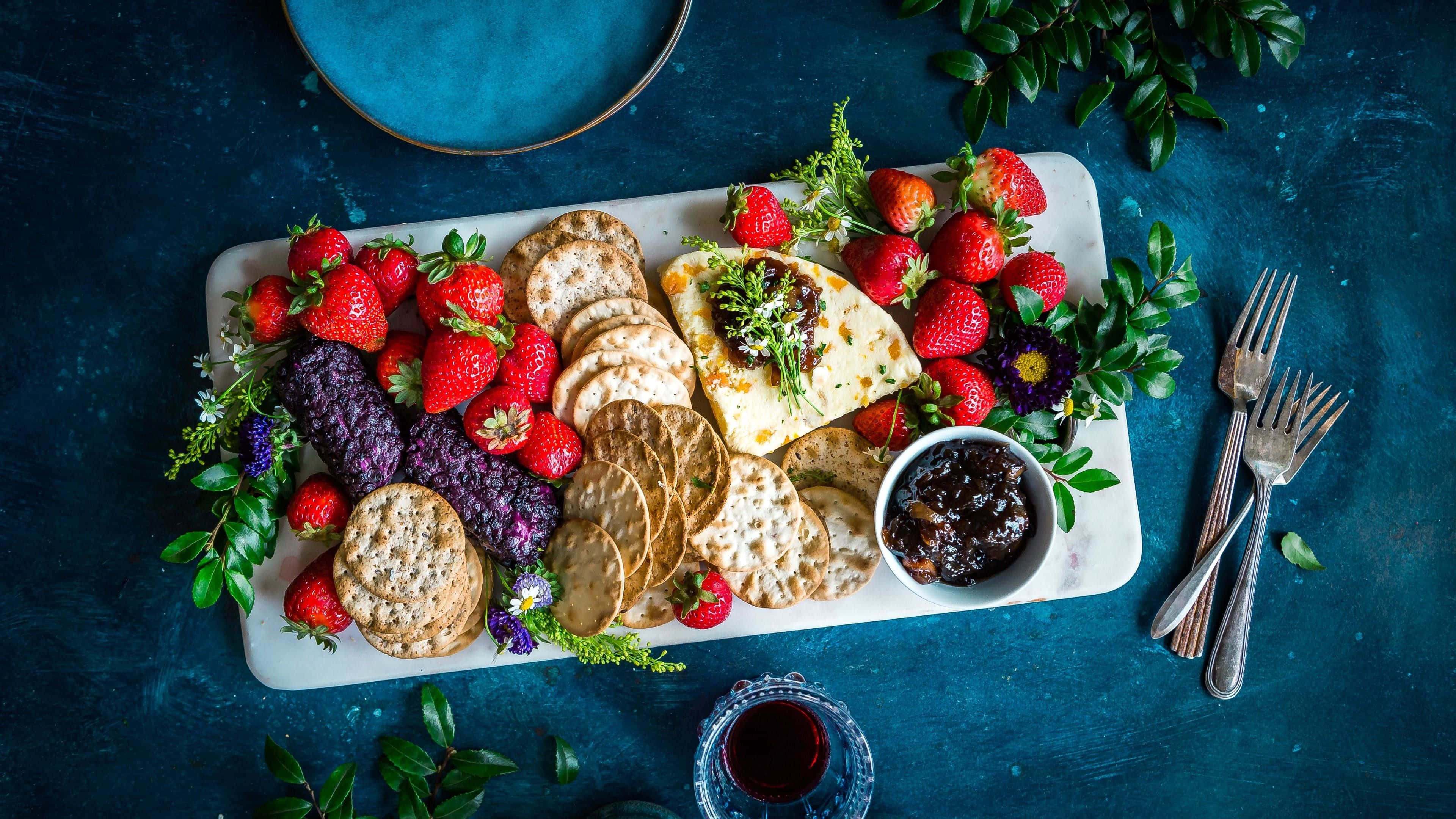 crackers 桌布 壁紙 — 一個充滿活力的熟食拼盤，上面擺放著草莓、餅乾、起司和果醬，放在白色托盤上，背景是深藍色紋理。