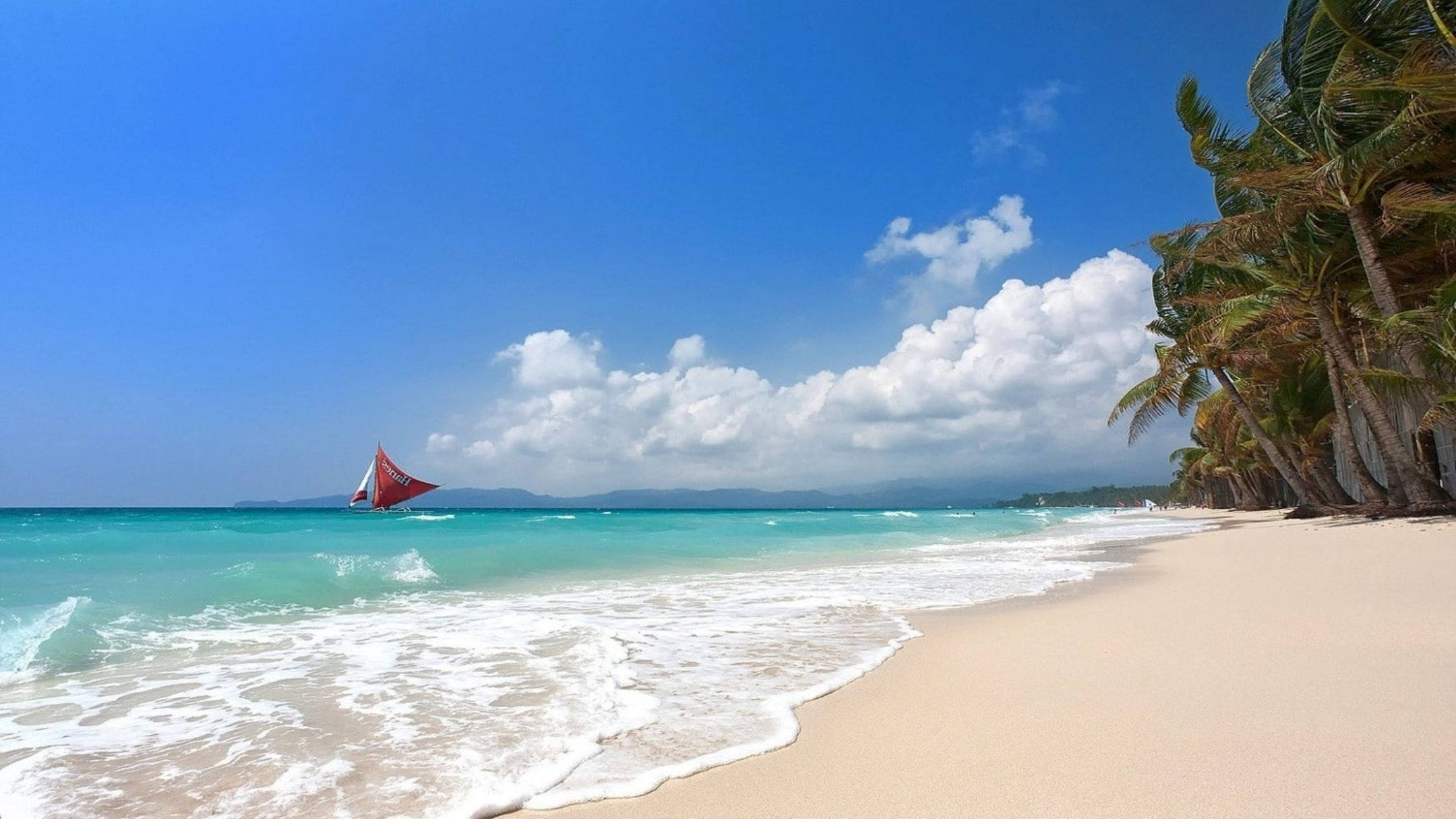 White Beach 桌布 壁紙 — 一個充滿活力的熱帶海灘，在明亮的藍天下，白色沙灘上翻湧著碧綠色的海浪，天空點綴著蓬鬆的白雲。