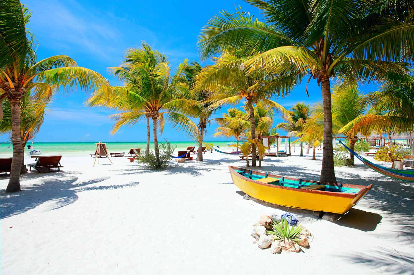 Mexican Beach 桌布 壁紙 — 一個充滿活力的熱帶海灘，有白色沙灘棕櫚樹和黃色小船，在清澈的藍天下。