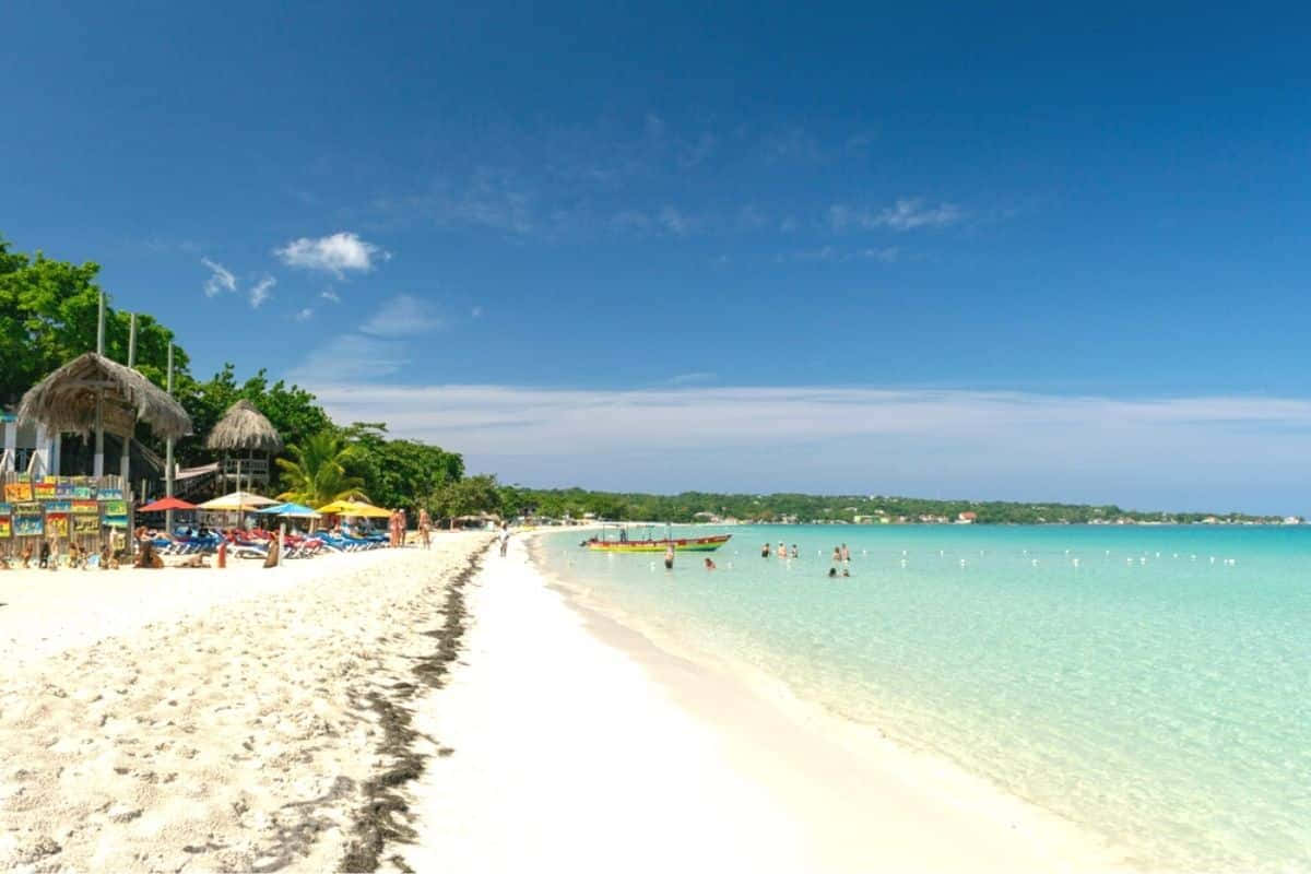 Jamaican Beach 桌布 壁紙 — 一個充滿活力的熱帶海灘，有白色沙灘、碧綠海水和色彩繽紛的遮陽傘，在清澈的藍天下。