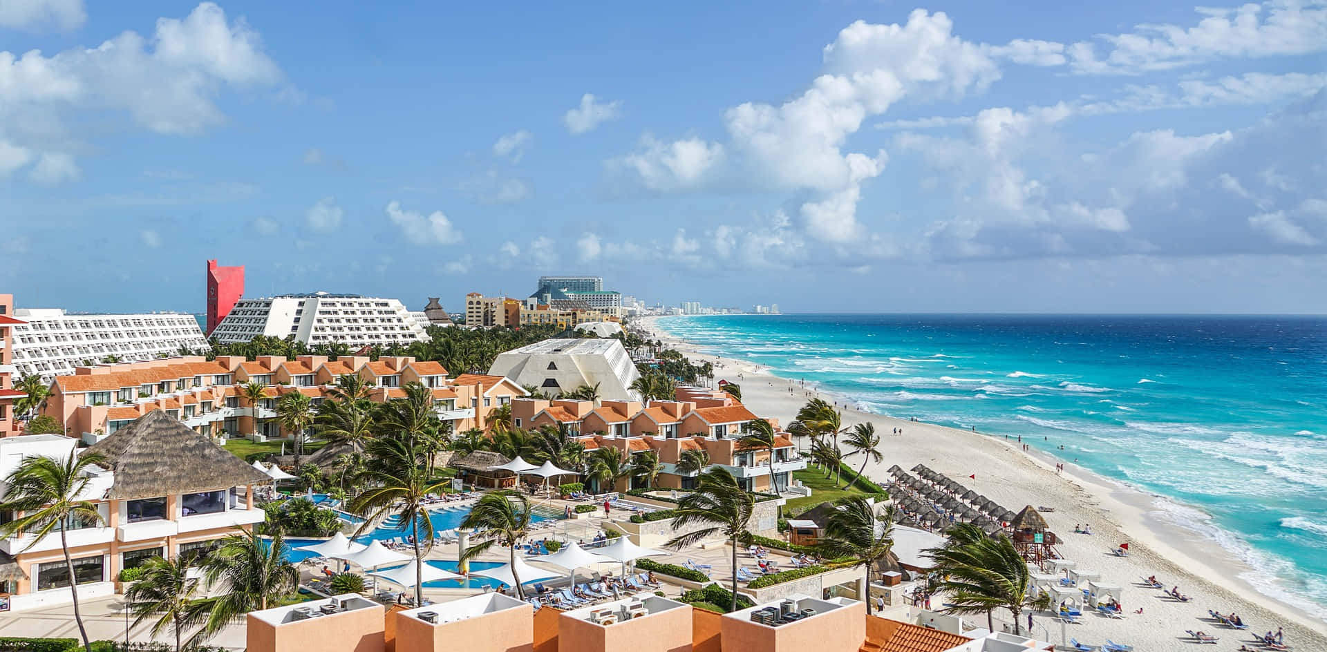 Cancun 桌布 壁紙 — 一個充滿活力的熱帶海灘度假村，擁有碧綠的海水和棕櫚樹，在明亮的藍天和蓬鬆的白雲下。