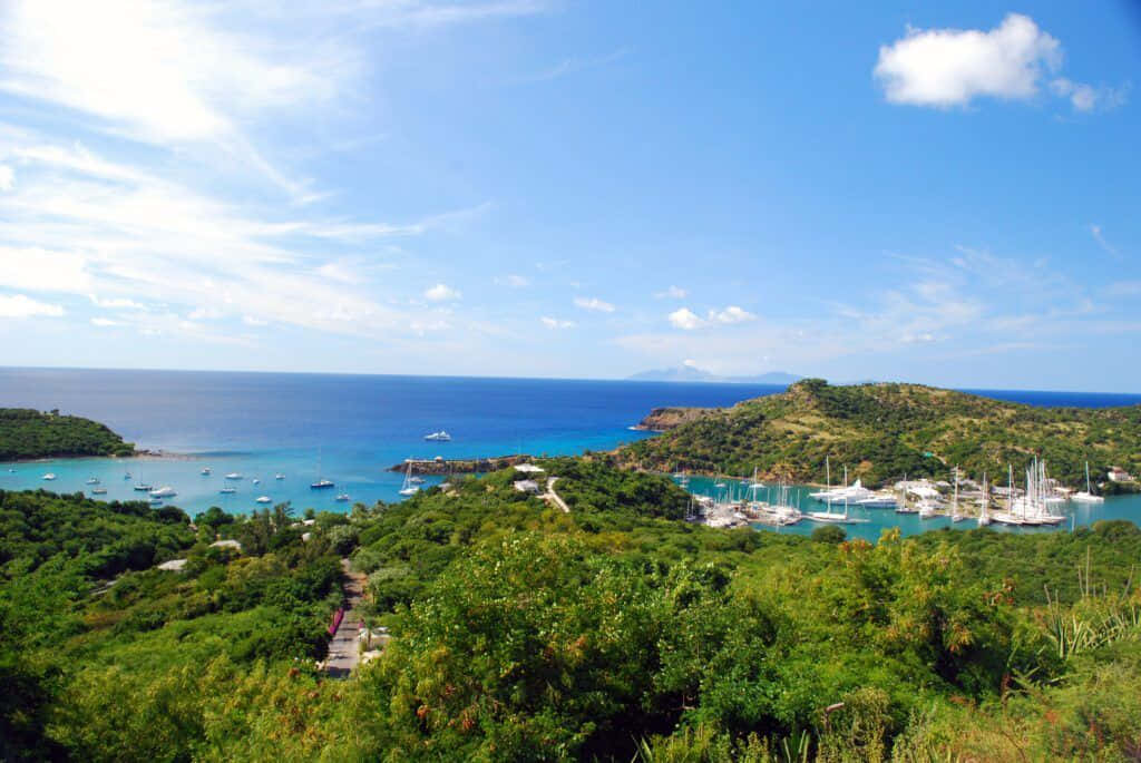 Caribbean Island 桌布 壁紙 — 一個充滿活力的熱帶海灣，碧綠的海水點綴著帆船，坐落在茂密的綠色山丘之間，上方是明亮的藍天。