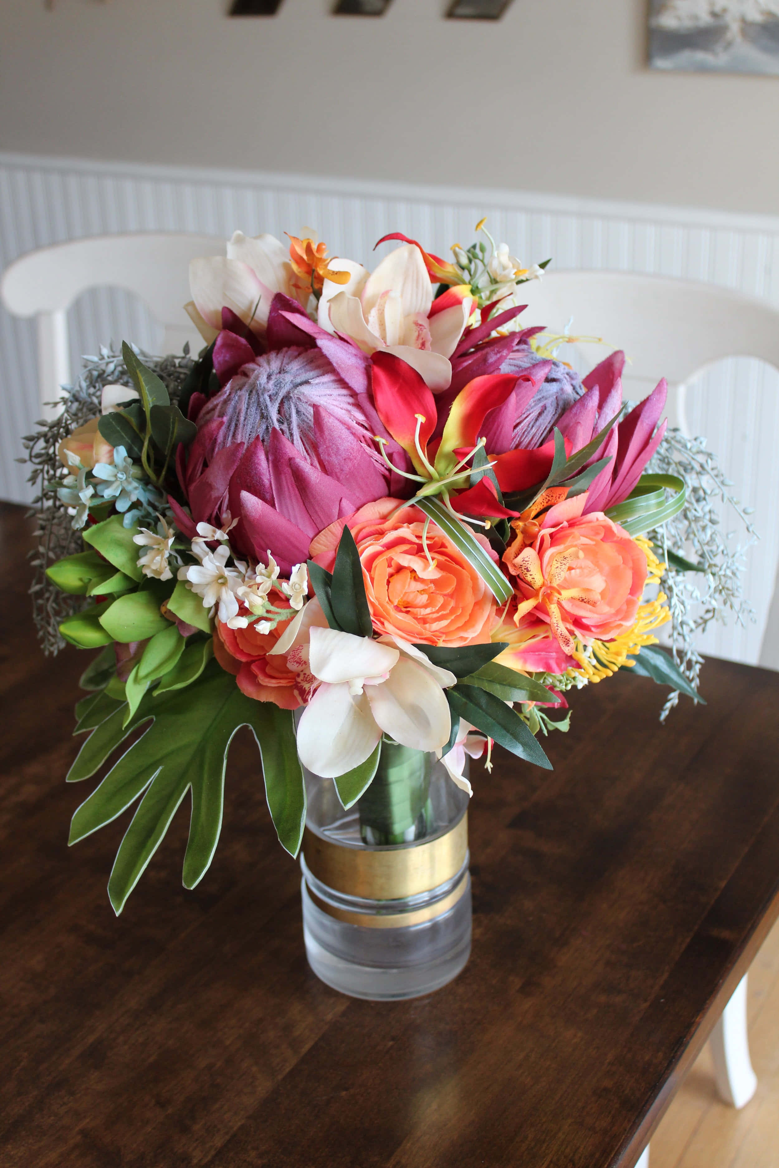 Wedding Bouquet 桌布 壁紙 — 一個充滿活力的熱帶花卉佈置，包括粉紅色帝王花、橙色玫瑰和白色蘭花，放在深色木桌上的玻璃花瓶裡。