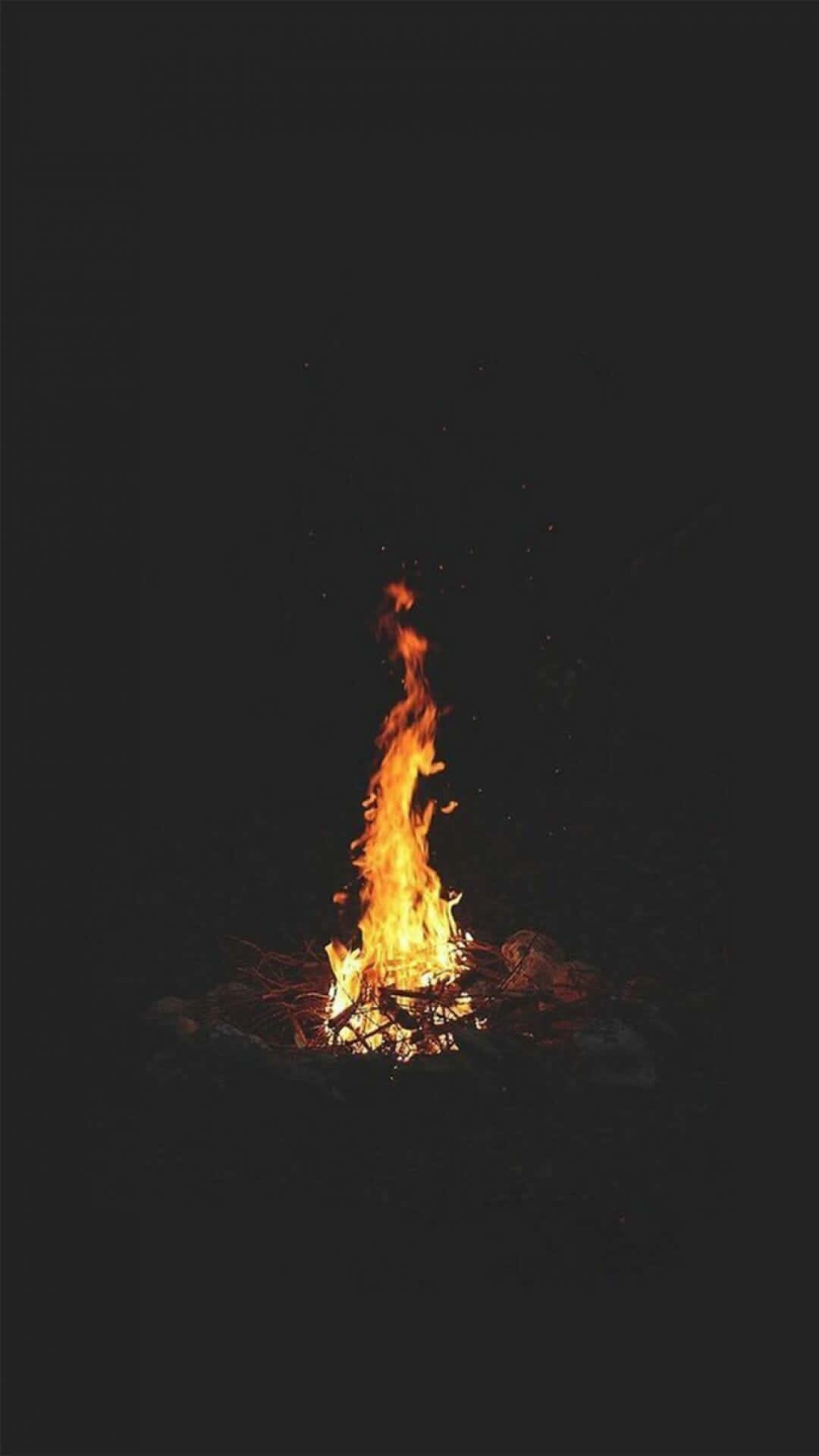 火焰動畫 桌布 壁紙 — 一個充滿活力的營火在漆黑的夜空中明亮地燃燒，將溫暖的橙色光芒投射到周圍的岩石上。