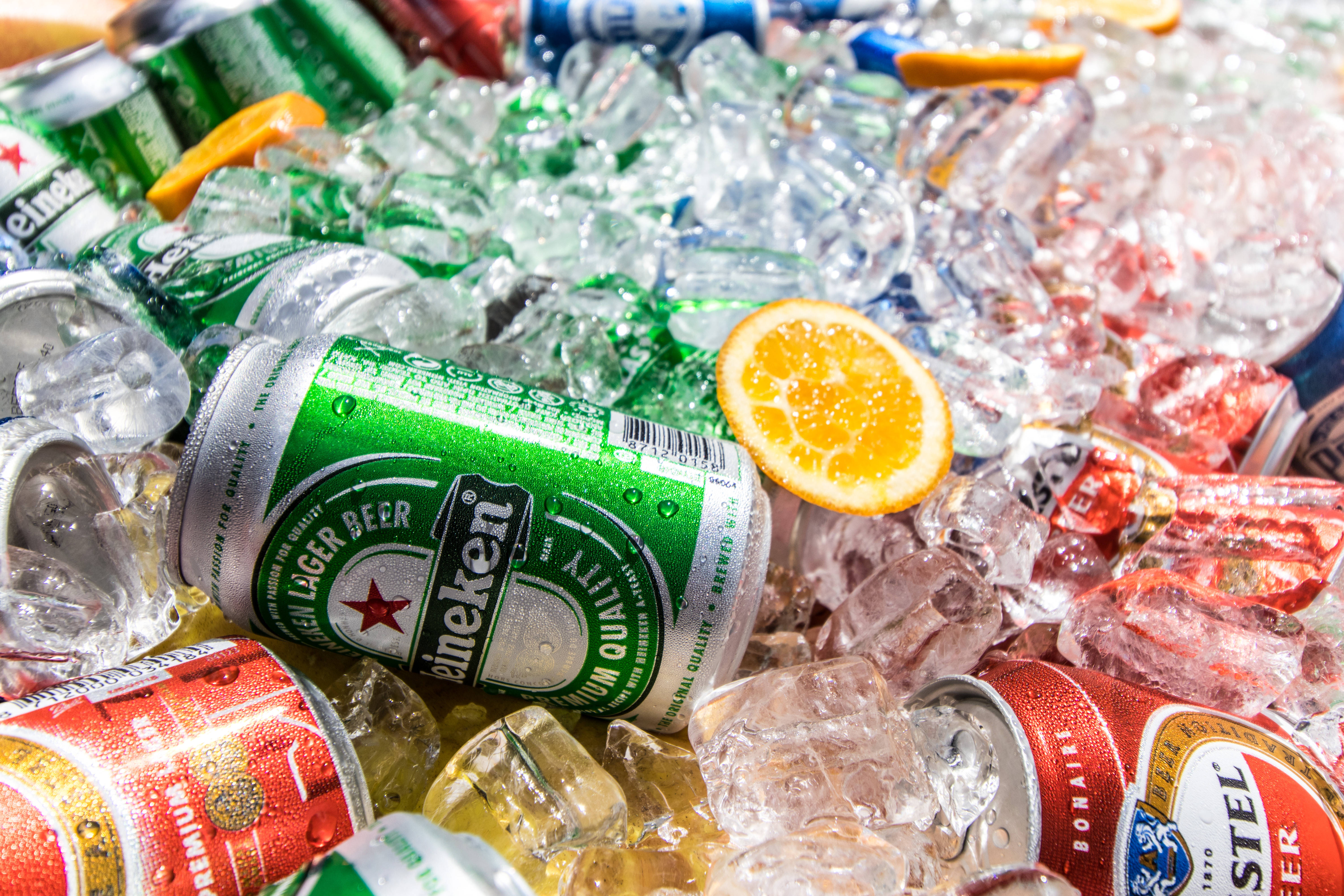 cube 桌布 壁紙 — 一個充滿活力的特寫，冰涼的啤酒罐依偎在閃閃發光的冰塊中，配上一片鮮亮的橙片。