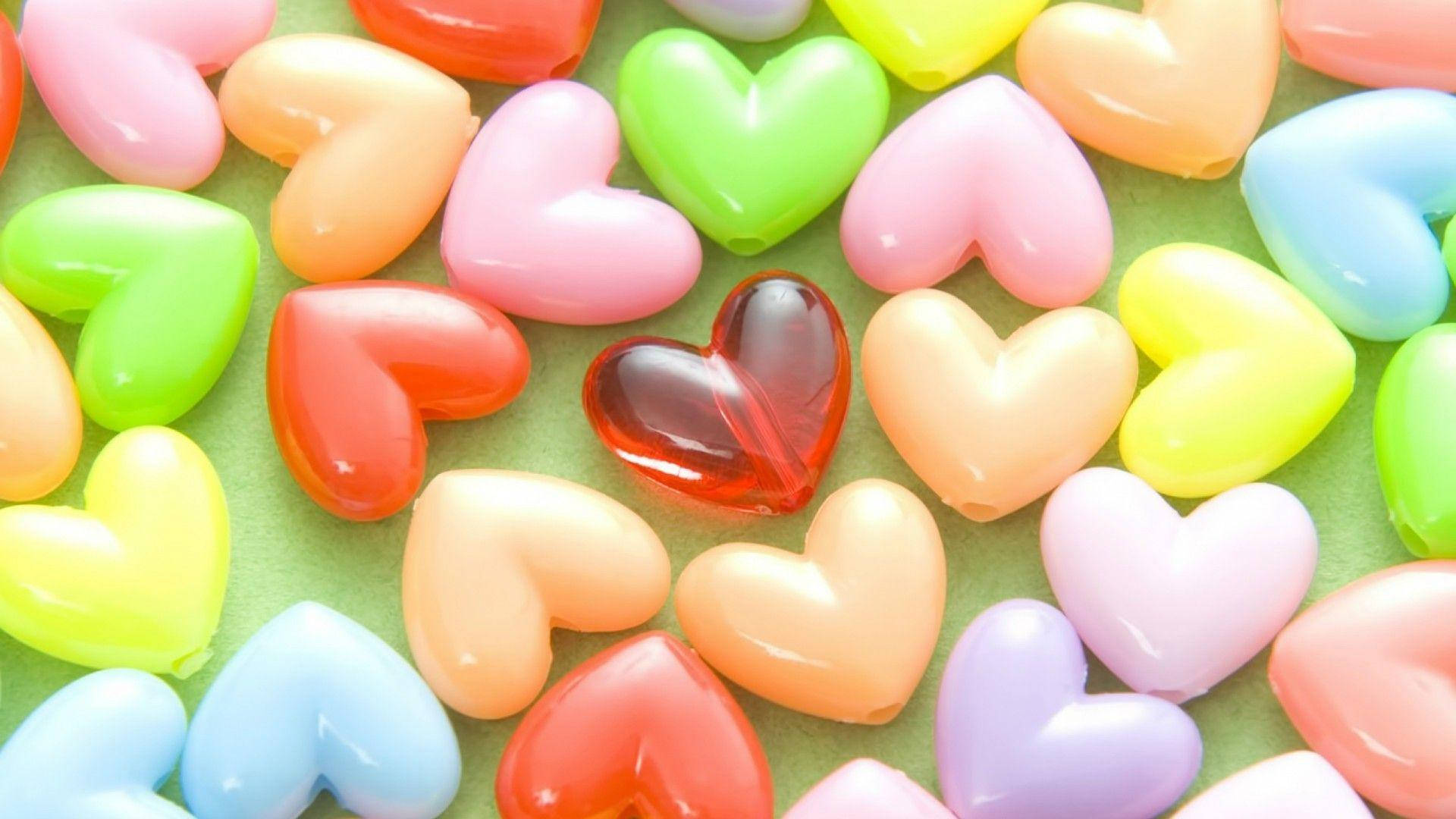 love full HD 桌布 壁紙 — 一個充滿活力的特寫，呈現出粉彩彩虹色調的光澤心形糖果散落在柔軟的綠色表面上。